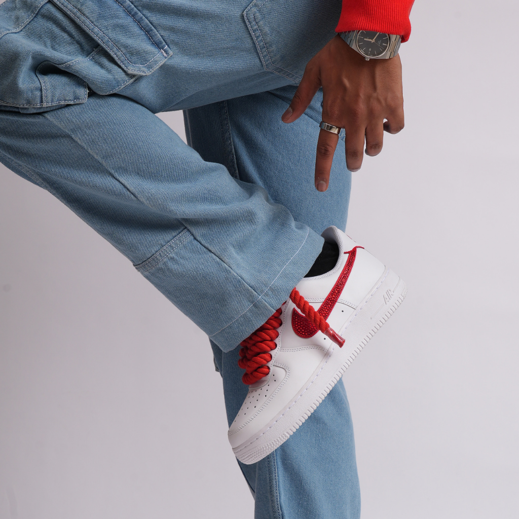 White sneaker with red laces and red swoosh, worn with light blue jeans and a watch.