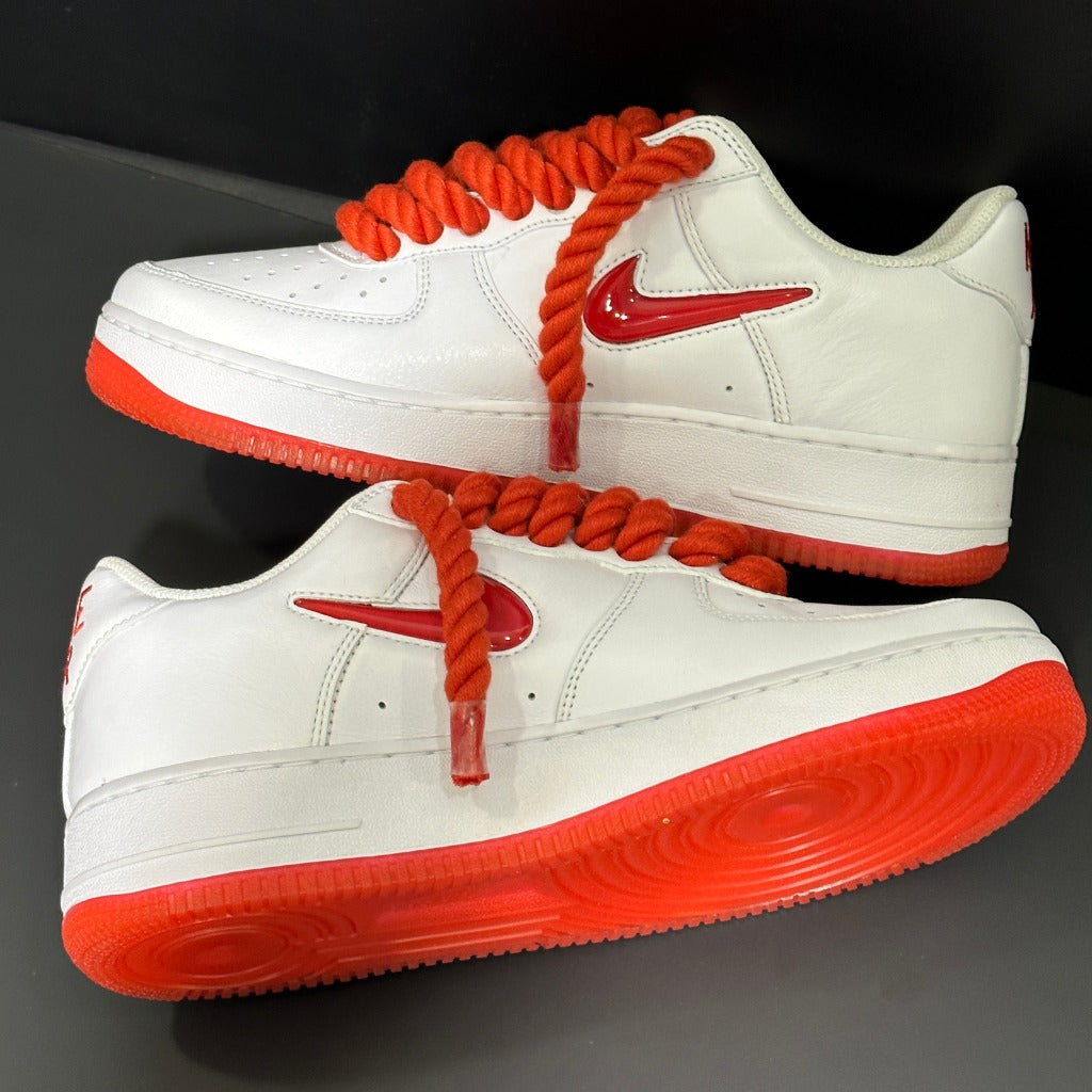 White low-top sneakers with bright red soles, thick red laces, and red Nike Swoosh logo