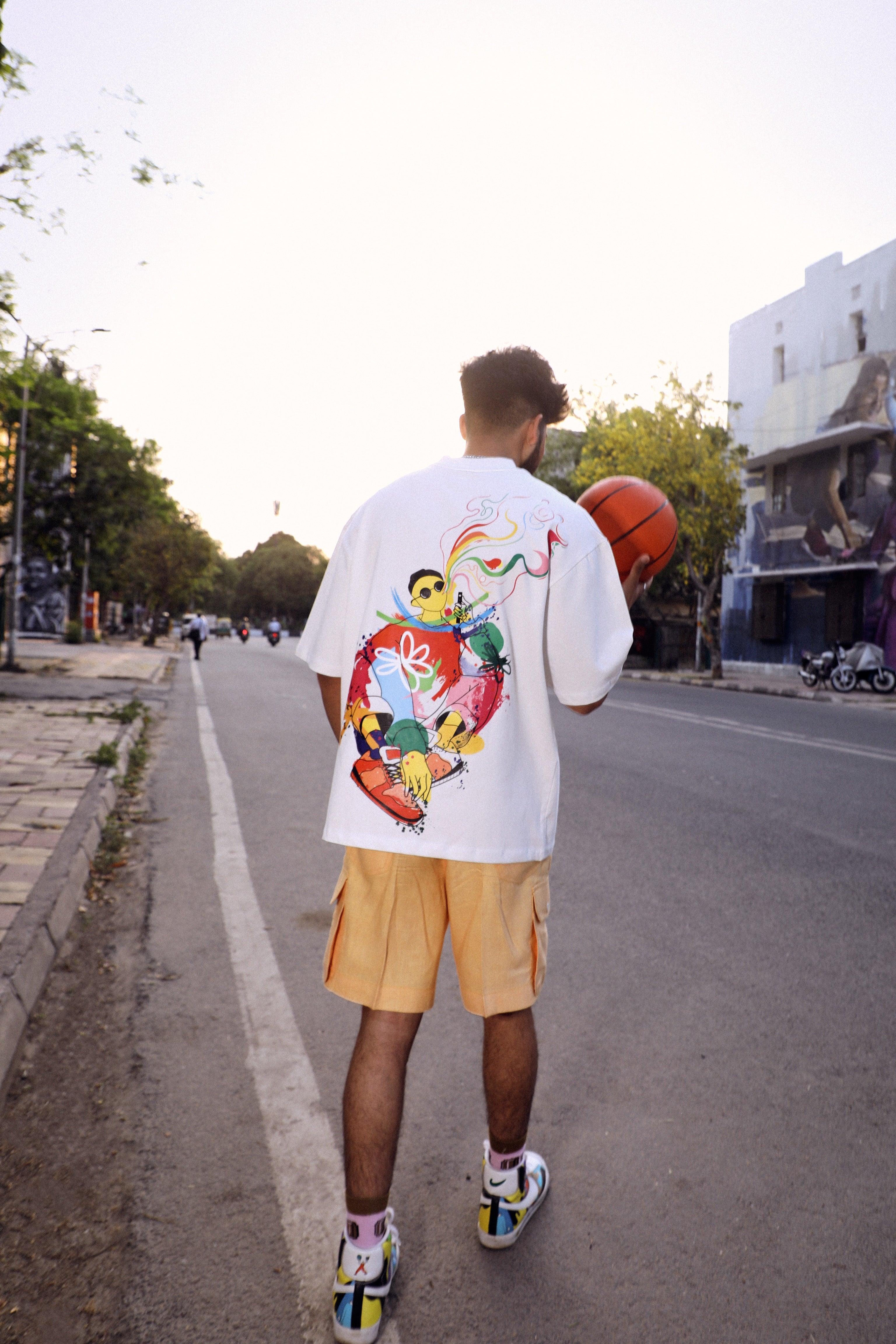 Man in streetwear with graphic t-shirt, orange shorts, and colorful sneakers holding basketball