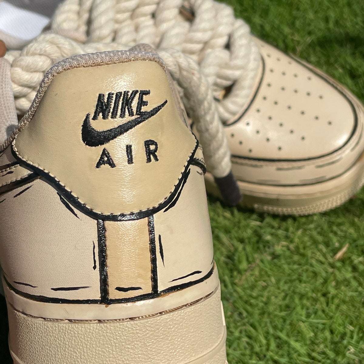 Beige Nike Air sneaker with black outlined details on green grass, close-up view