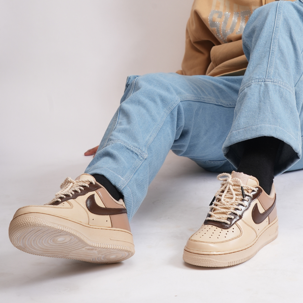 Person wearing light blue jeans and beige brown sneakers with black swoosh logo