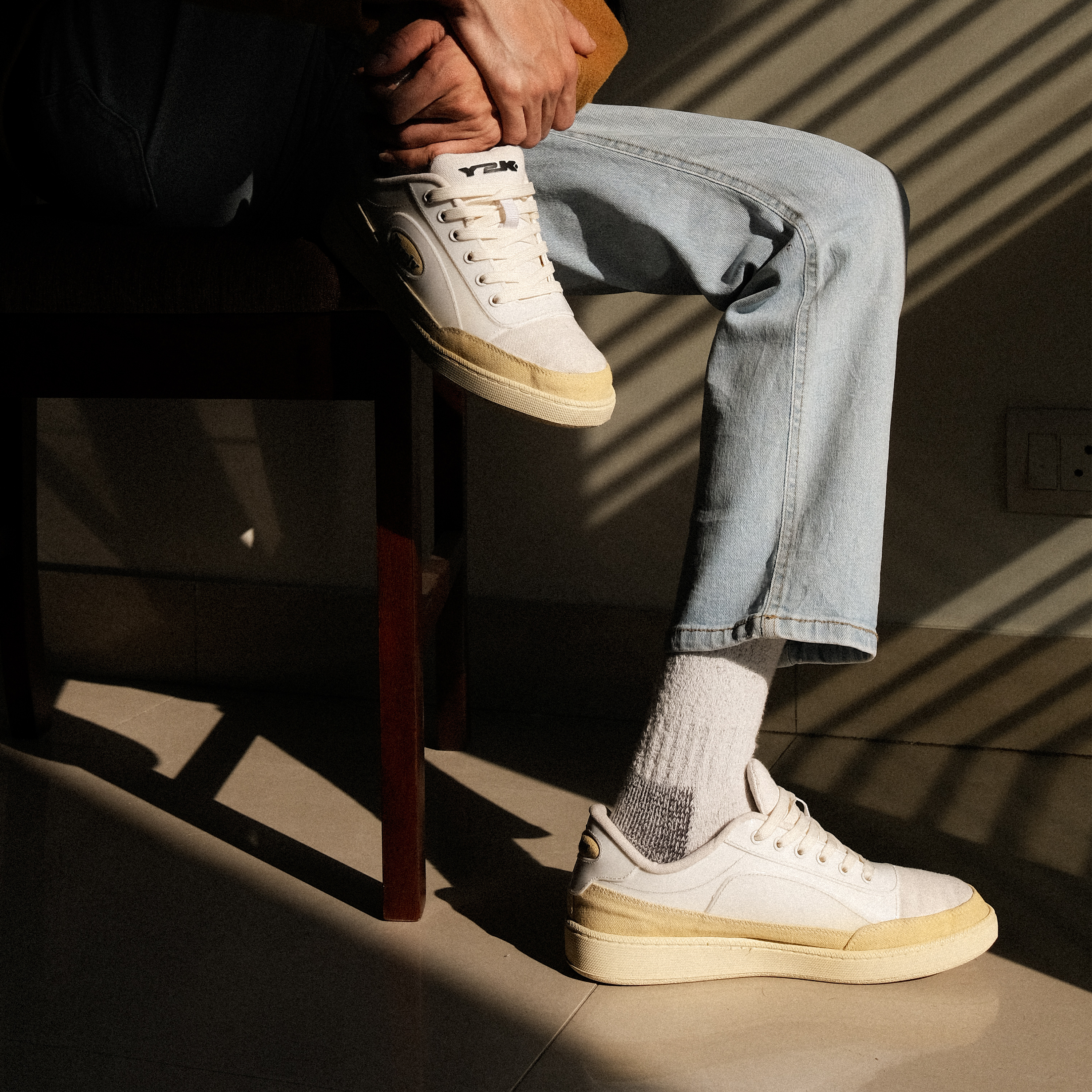 Person wearing cream sneakers and light wash jeans sitting indoors in natural light