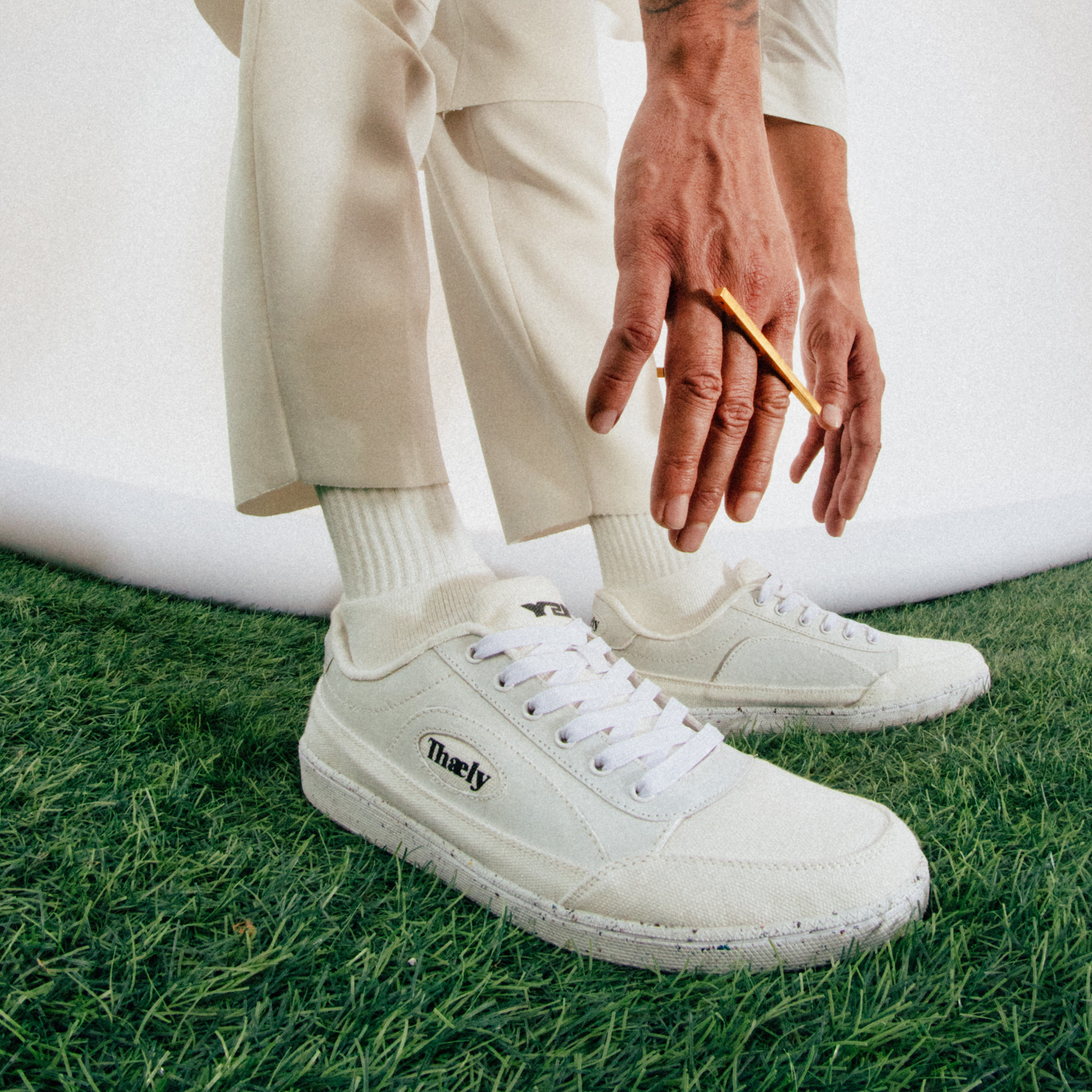 White streetwear sneakers with logo, worn with white pants and socks on green grass