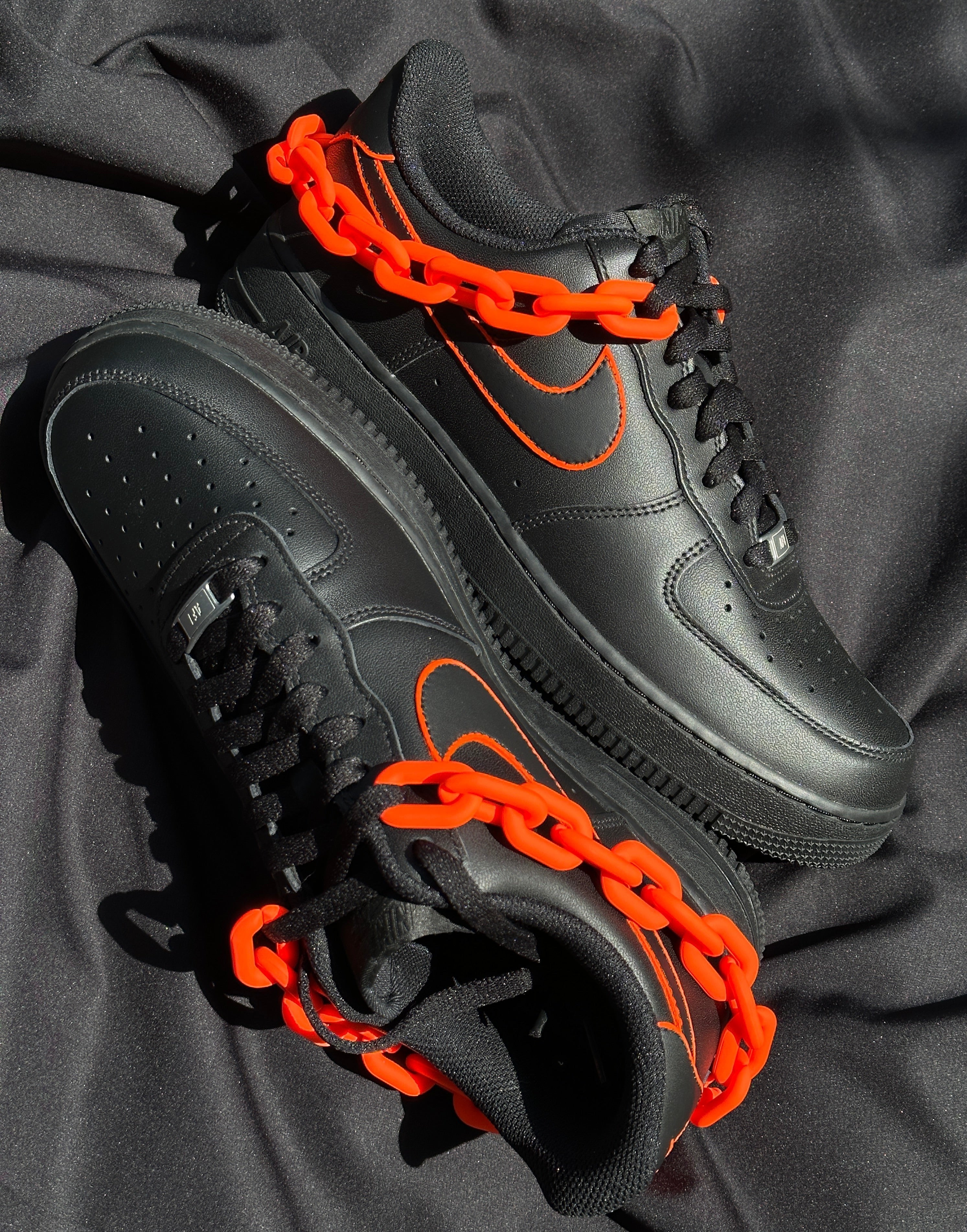 Black leather streetwear sneakers with orange details and orange chain on black fabric