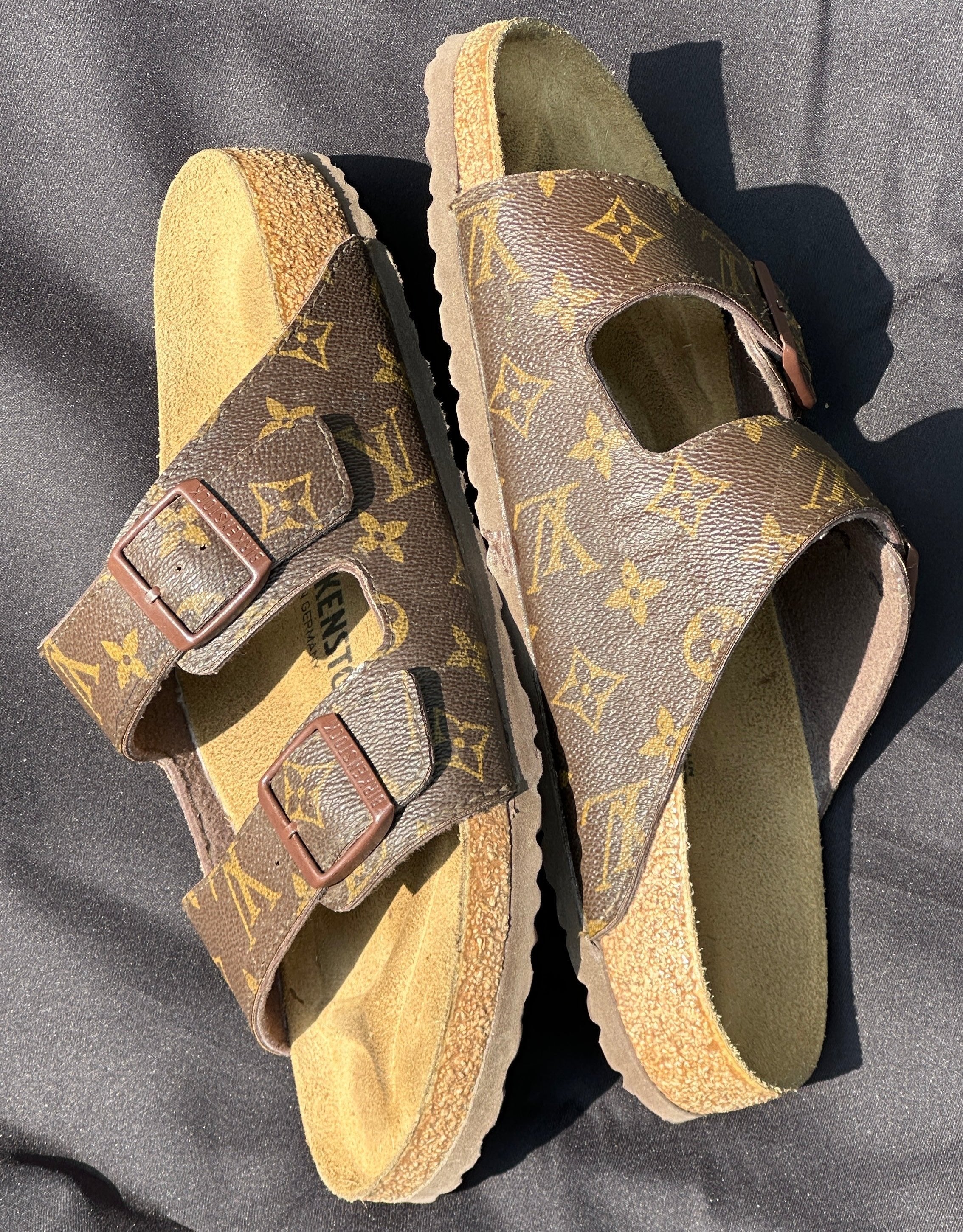 Brown designer slip-on sandals with gold monogram print and double straps on black fabric background