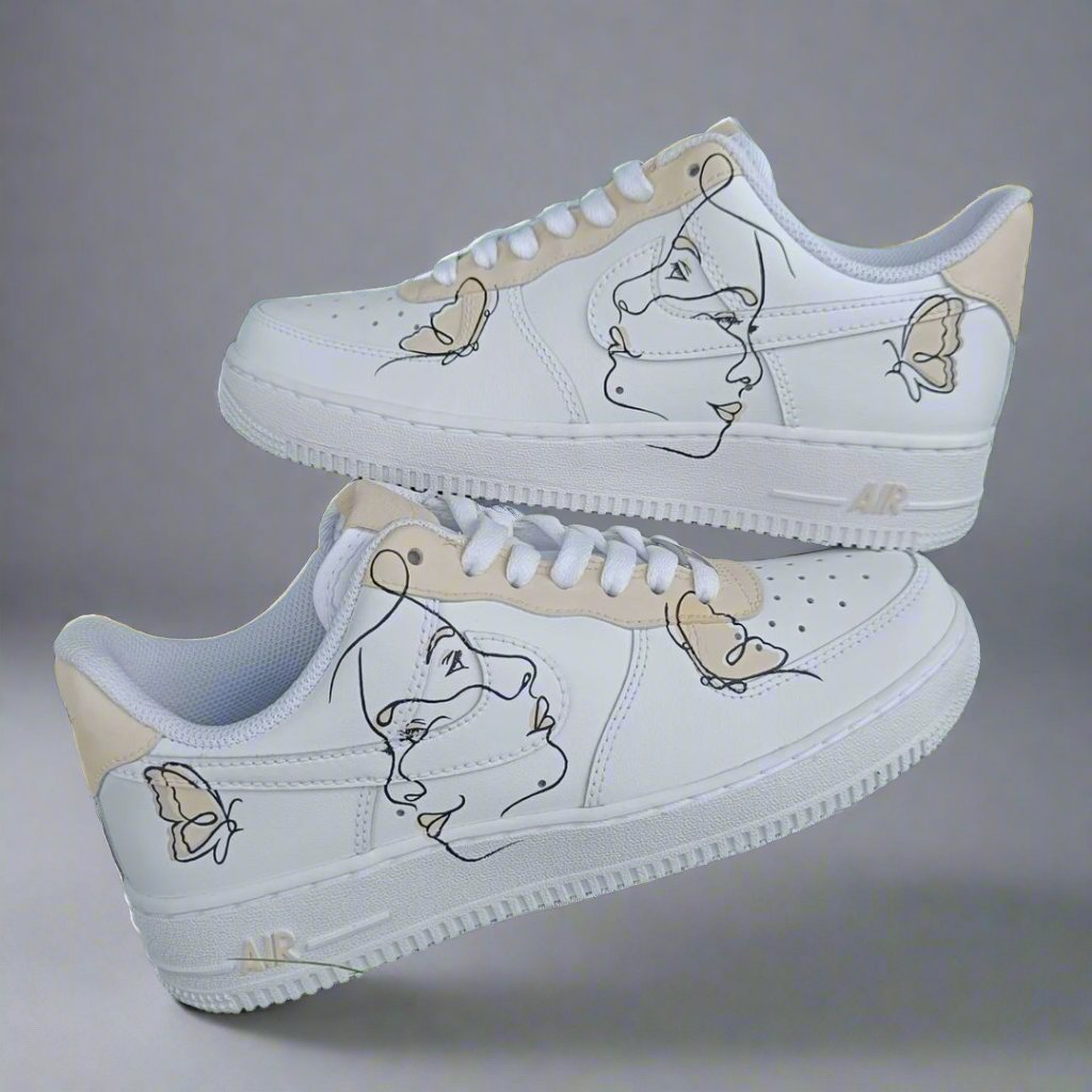 White custom Air Force 1 sneakers with abstract face and butterfly line art designs.