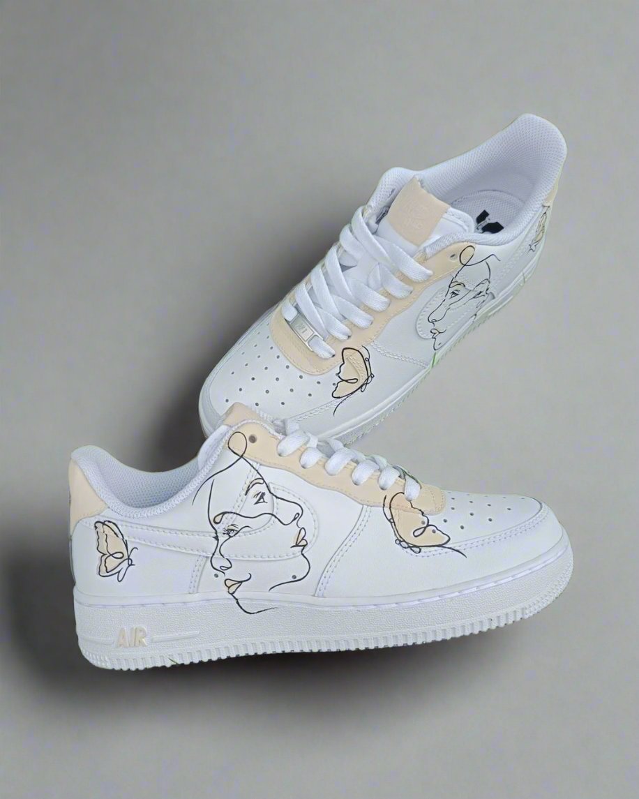 White Air Force 1 custom sneakers with abstract face and butterfly designs on the sides.