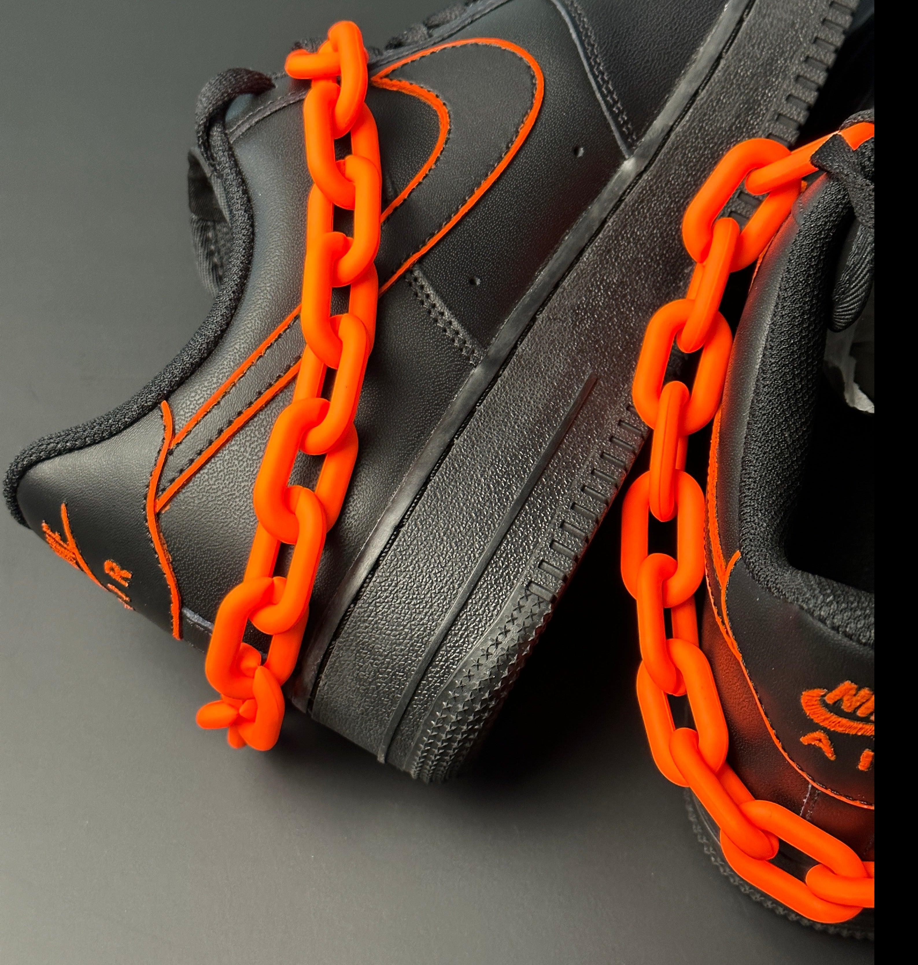 Black streetwear sneakers with orange stitching and bold orange chain detail on black background