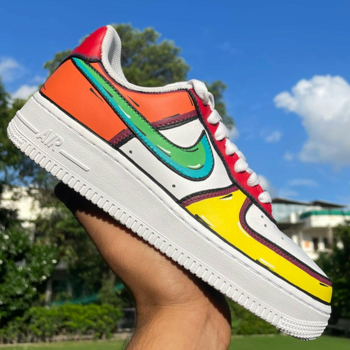 Colorful streetwear sneaker with cartoon-style details held outdoors against blue sky