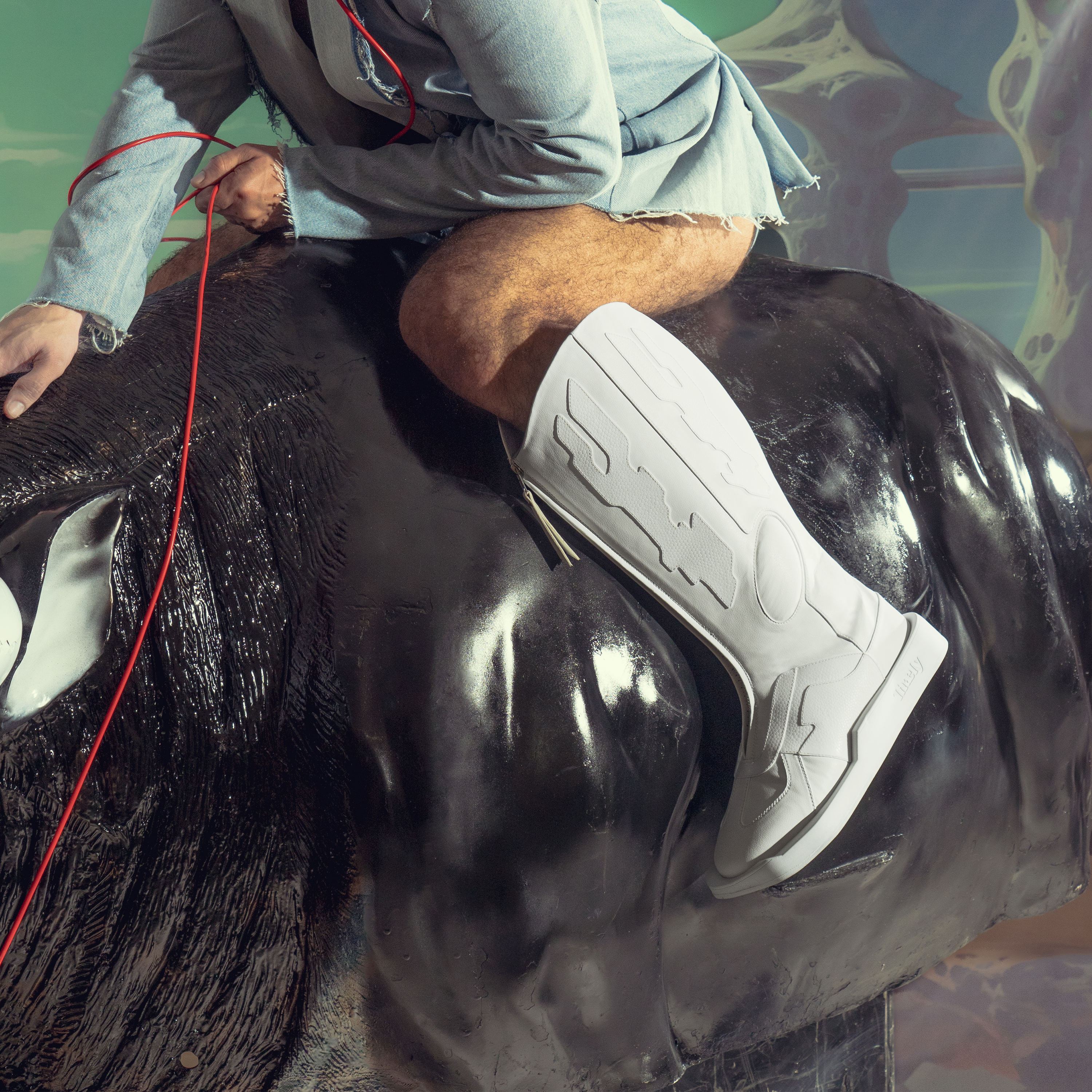 Person in distressed denim and white designer knee-high boots riding glossy black bull sculpture