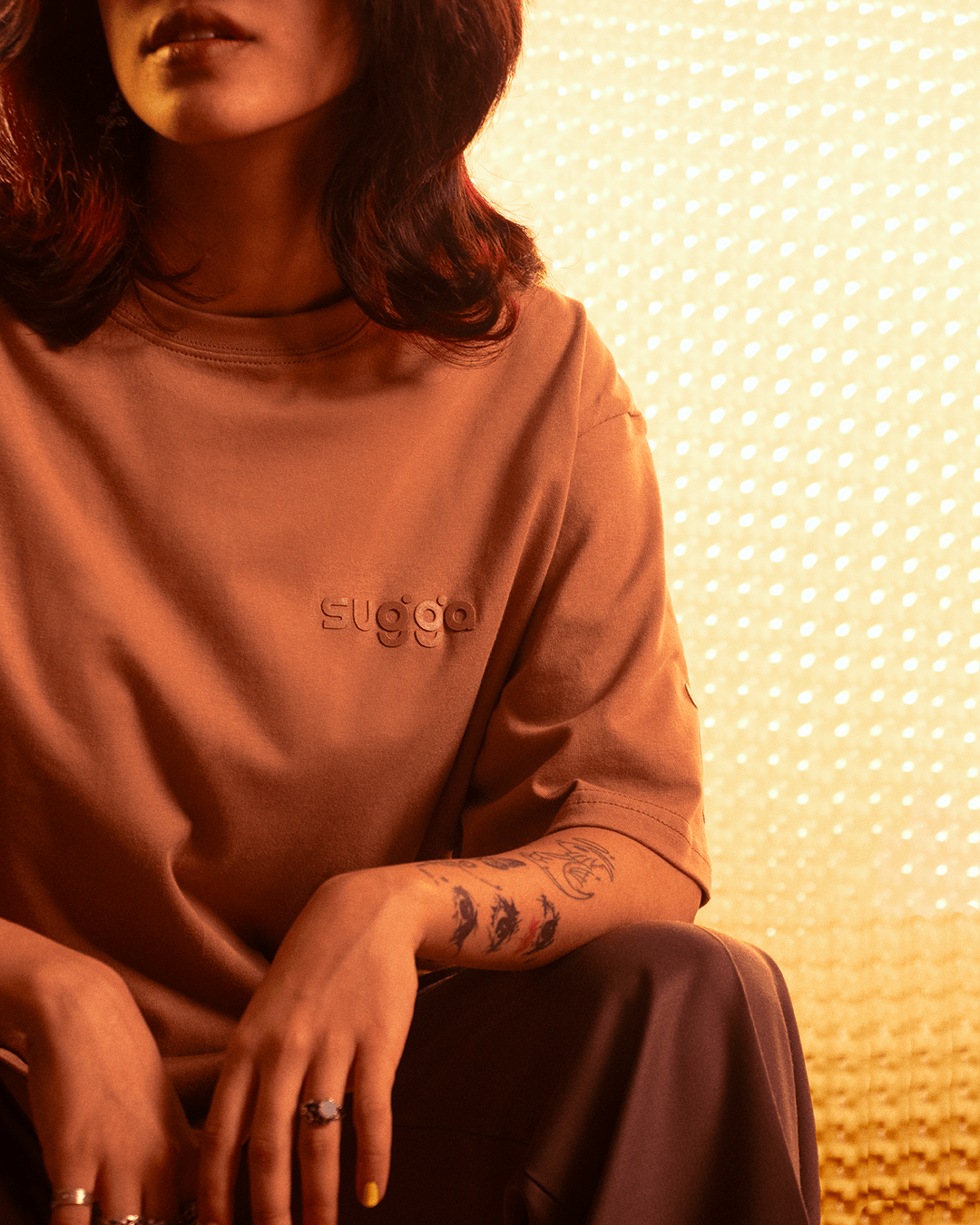 Woman wearing oversized brown streetwear t-shirt with subtle logo, tattoo and rings visible