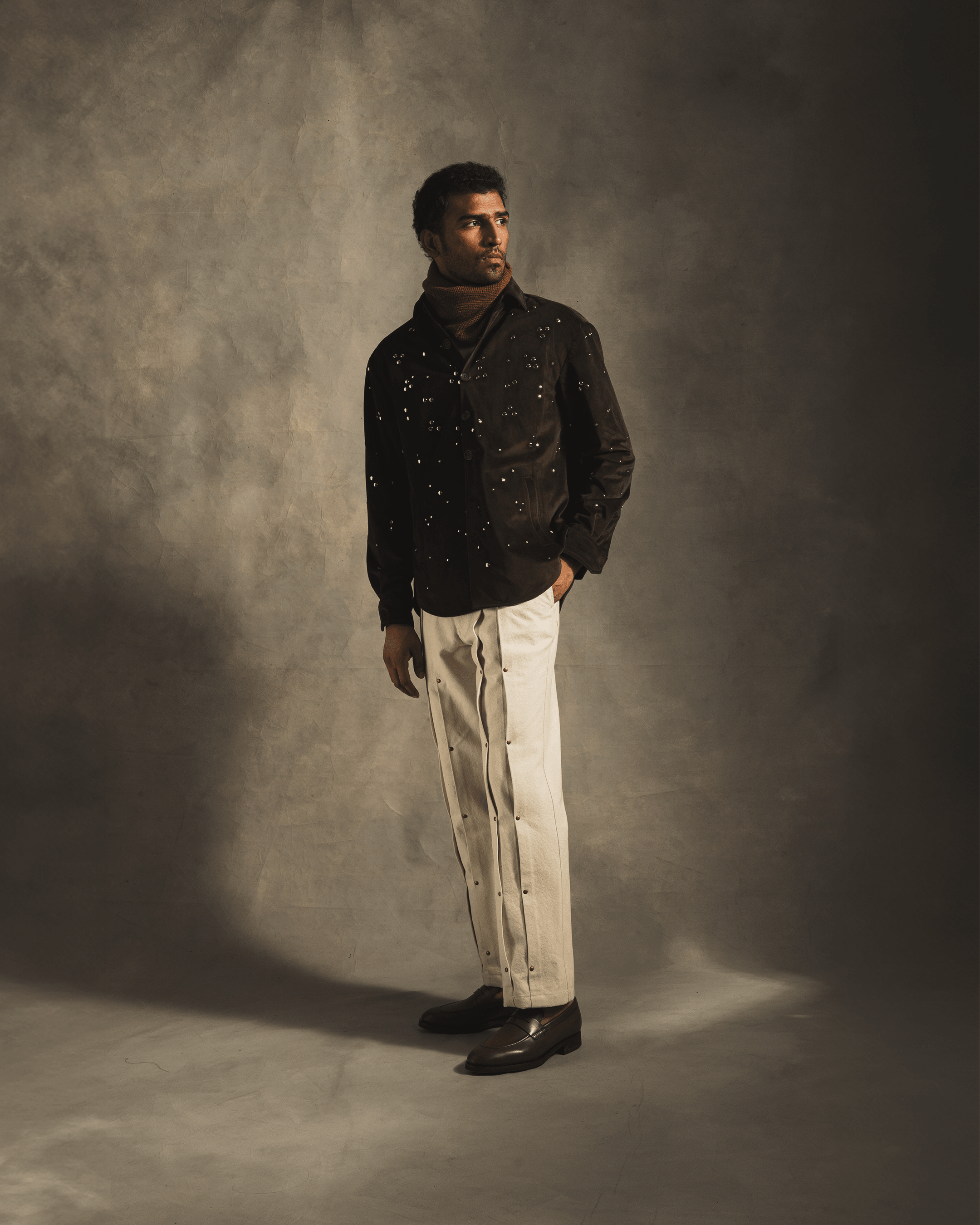Man modeling brown rivet shirt with metallic accents, cream pants and loafers in studio