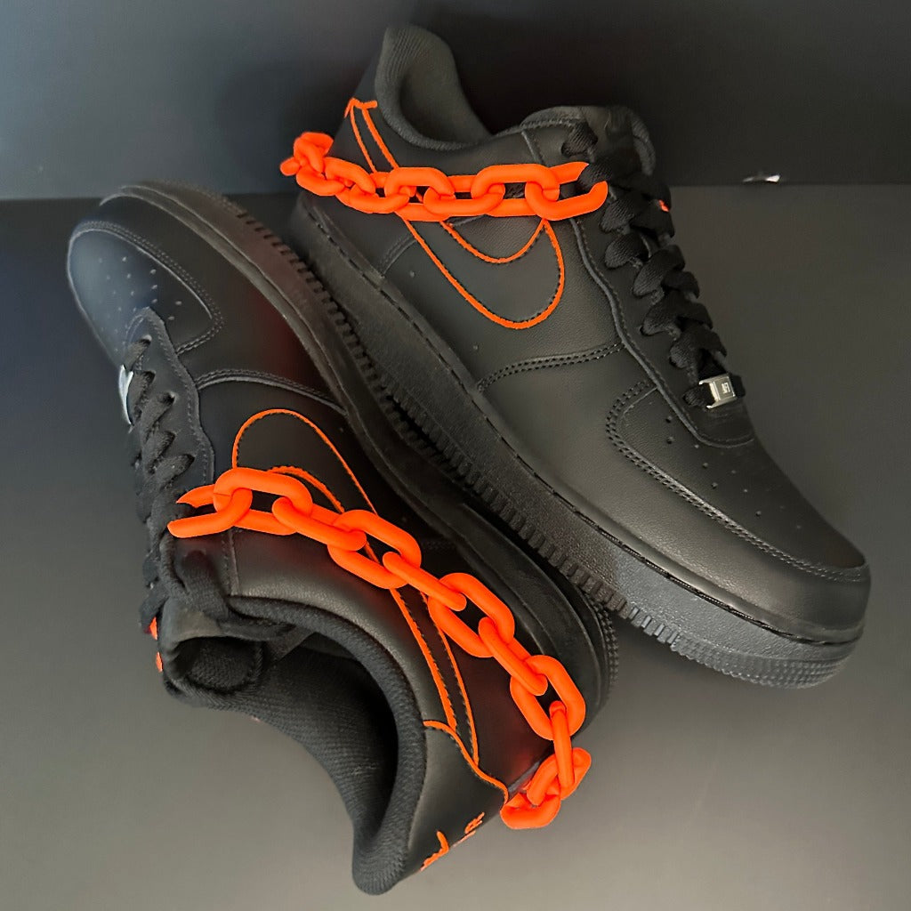 Black streetwear sneakers with orange stitching and chunky orange chain detail