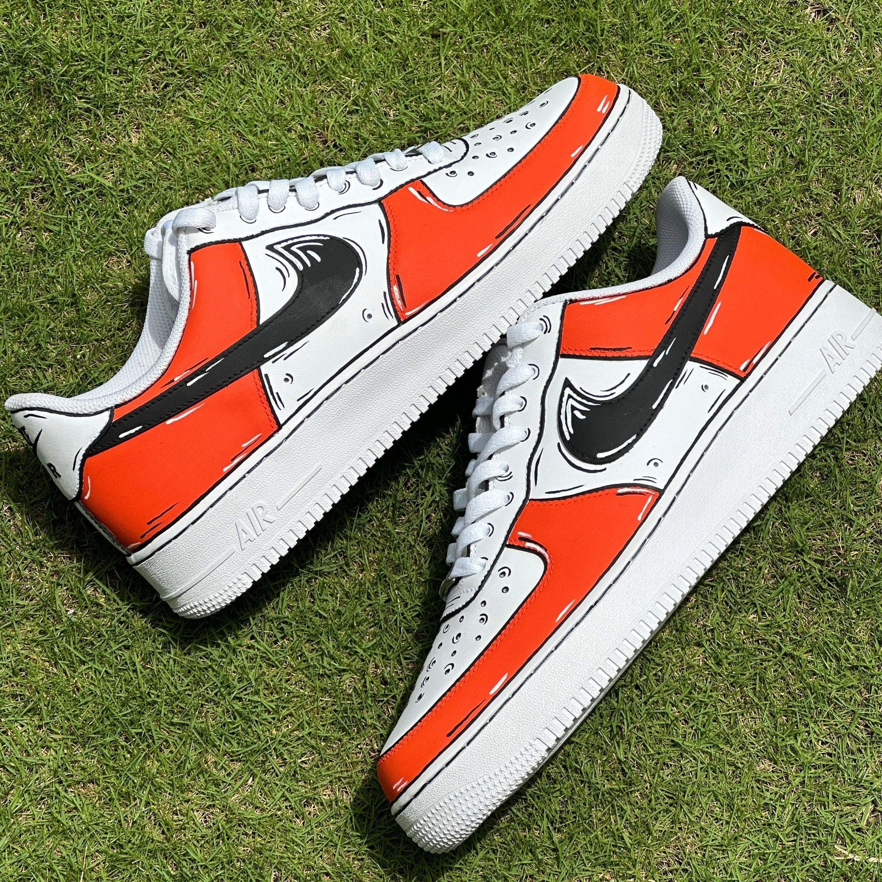 Custom white and orange low-top streetwear sneakers with black swoosh on grass