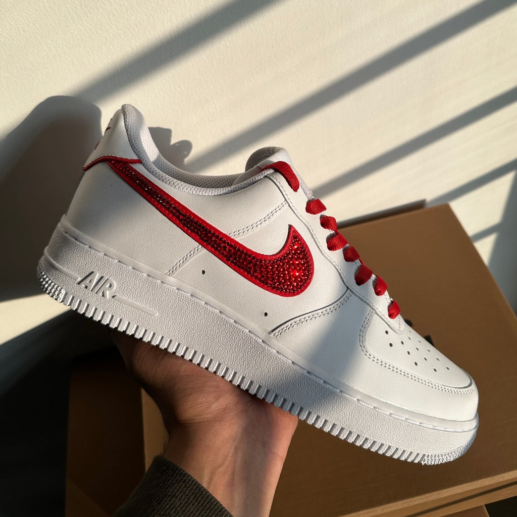 White sneaker with red jeweled swoosh and laces, streetwear footwear in hand, sunlight