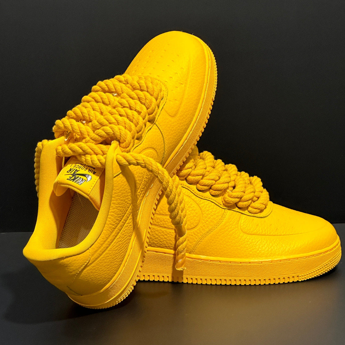 Bold yellow Nike Air Force 1 sneakers with chunky rope laces on a black background