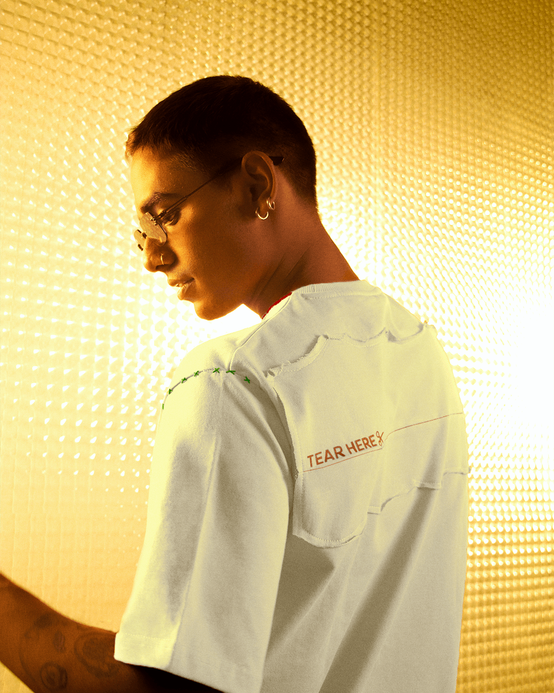 Man in white streetwear t-shirt with 'Tear Here' printed back, gold textured background