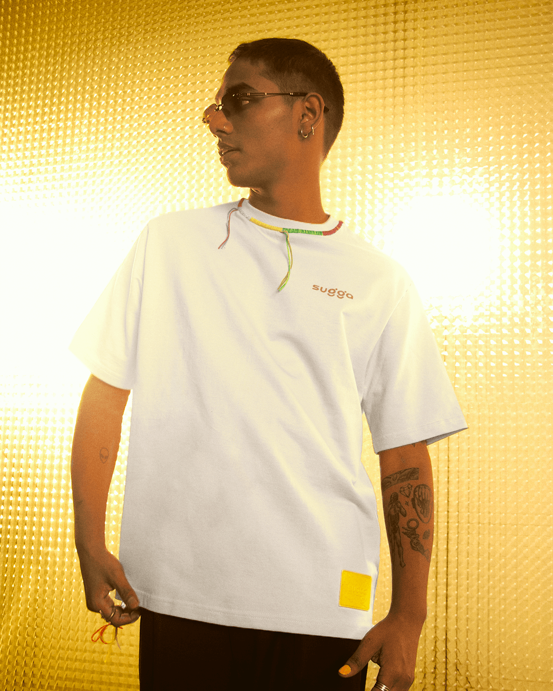 Streetwear model in a white graphic t-shirt with yellow patch and sunglasses, gold background