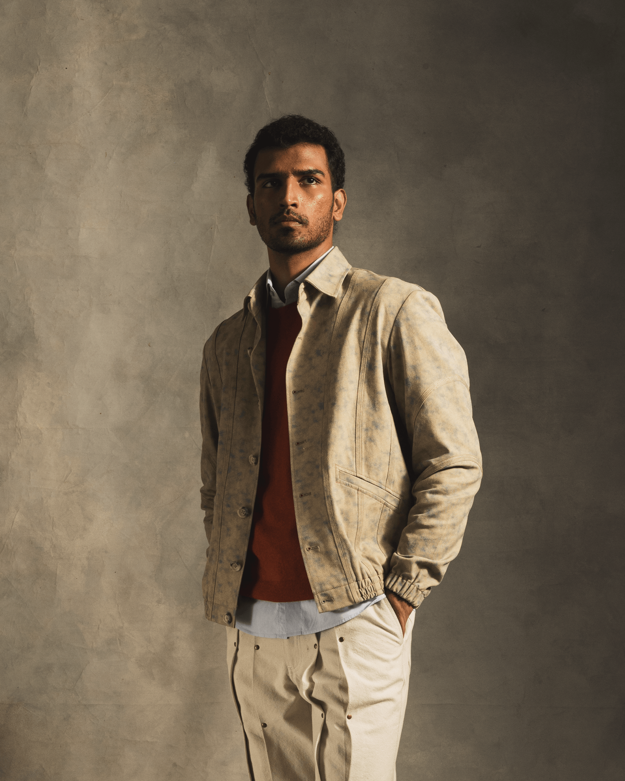 Man wearing a beige cloud-patterned streetwear jacket, red sweater, and cream pants