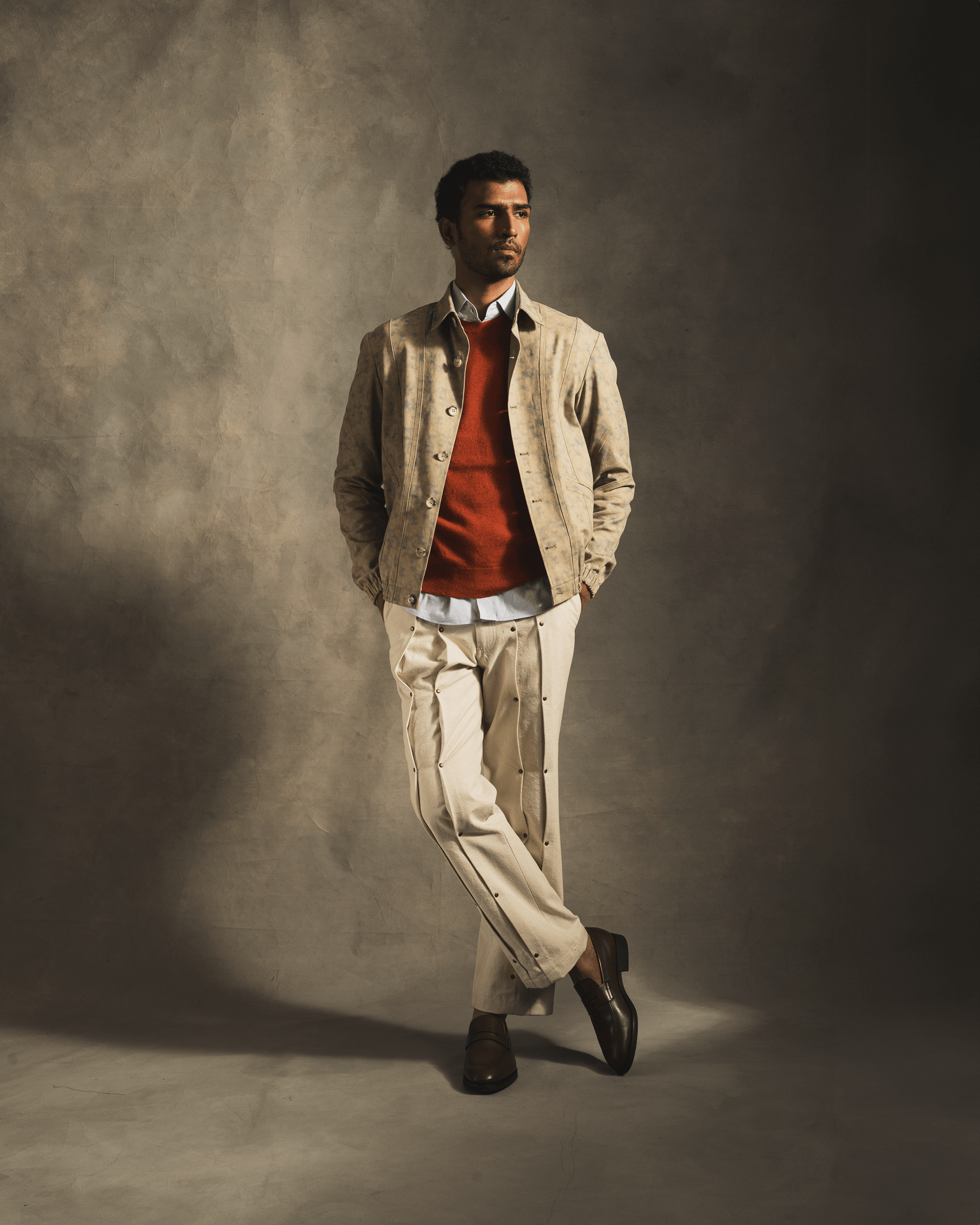 Man modeling contemporary streetwear with beige jacket, red sweater, cream pants, brown loafers