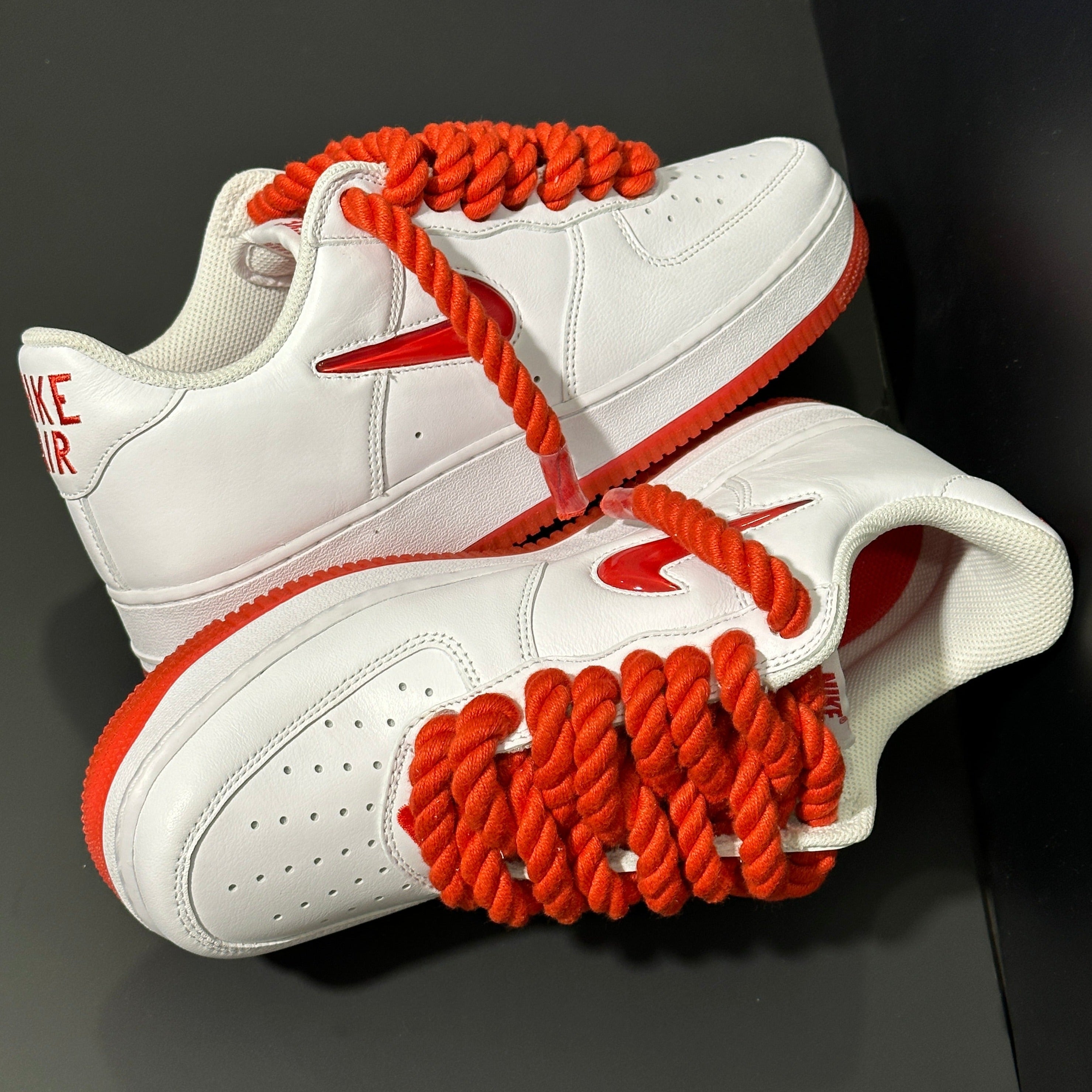 White and red low top sneakers with bold rope laces and red swoosh, streetwear style