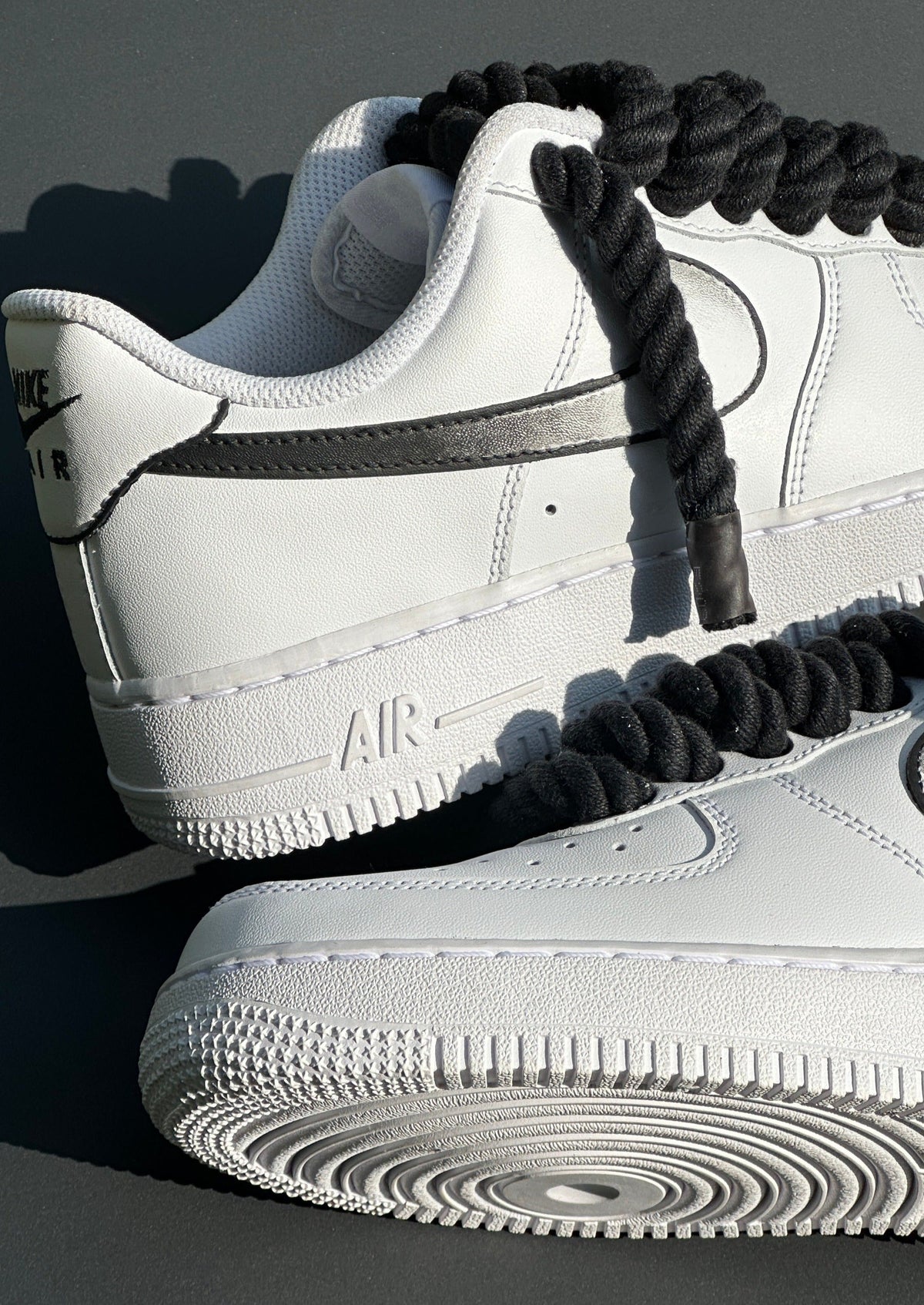 White Nike Air Force 1 sneakers with thick black laces and black Swoosh logo, streetwear style