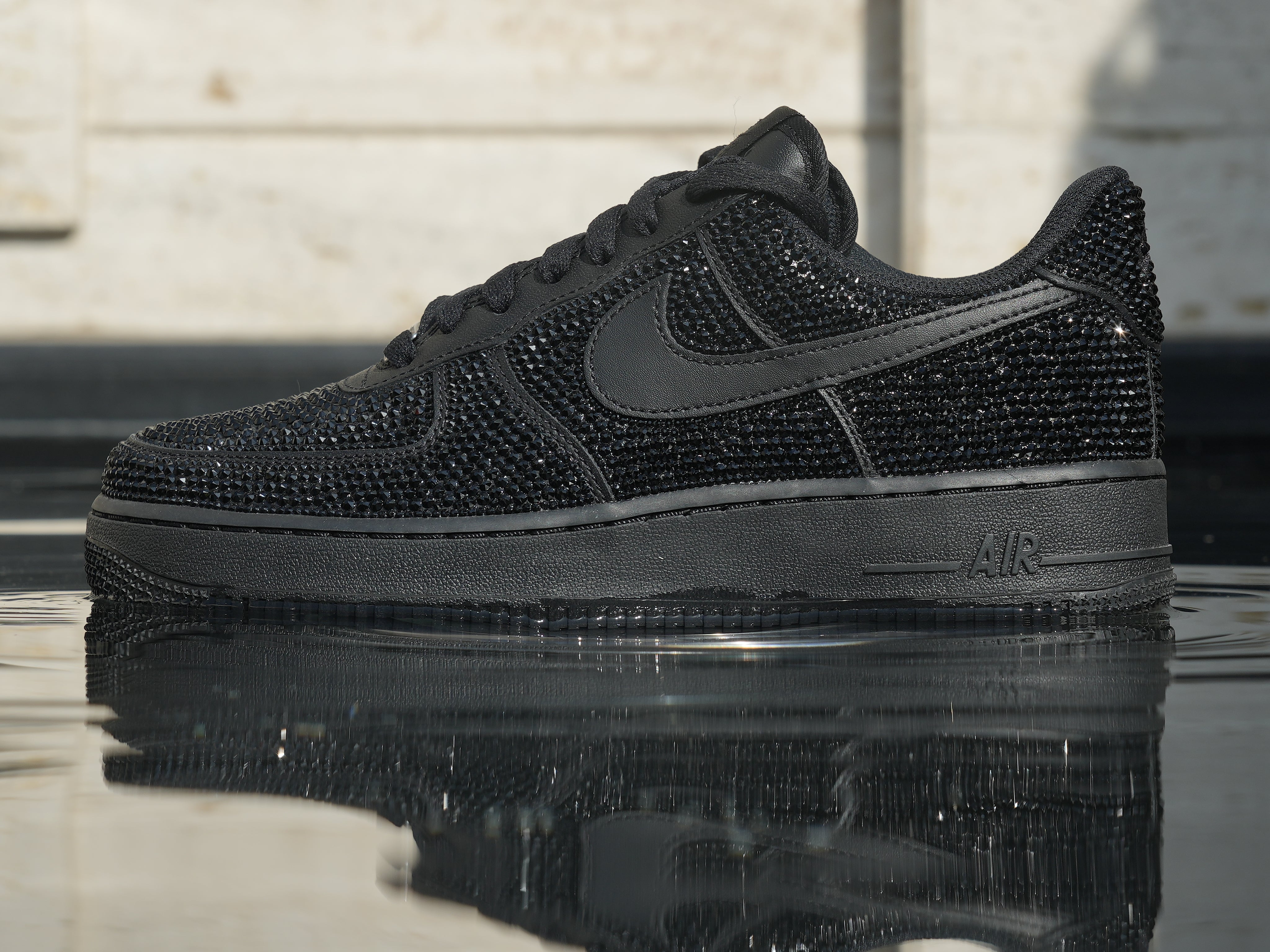 Black luxury sneaker with rhinestone embellishments reflected on water