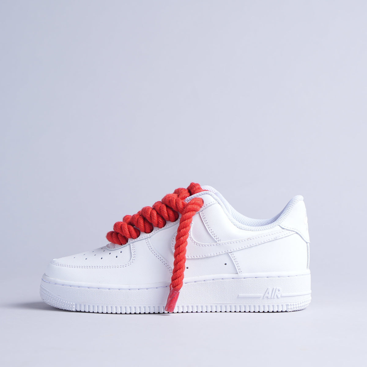 White leather sneaker with oversized red rope laces on a plain background