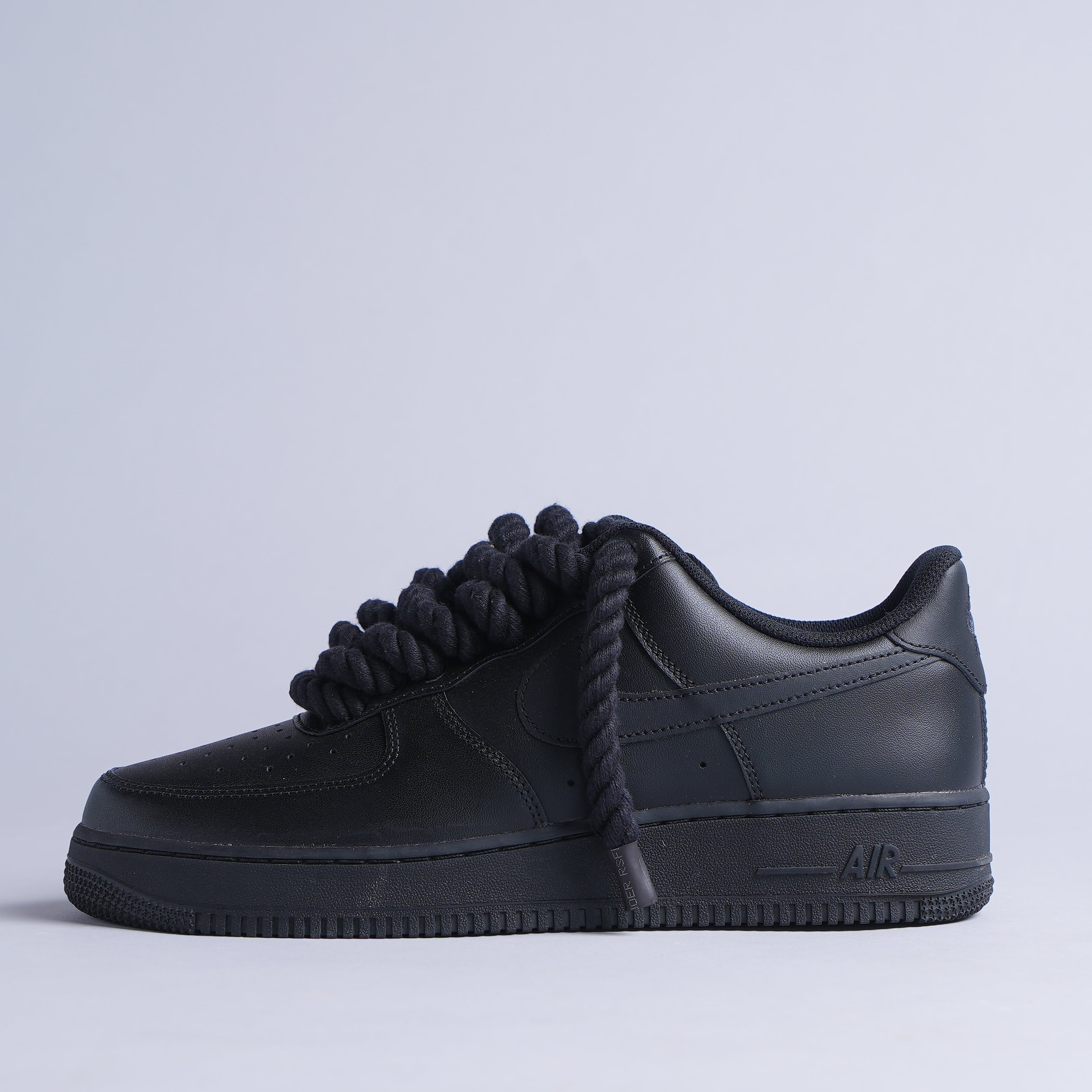 All-black sneaker with oversized rope shoelaces on a plain studio background