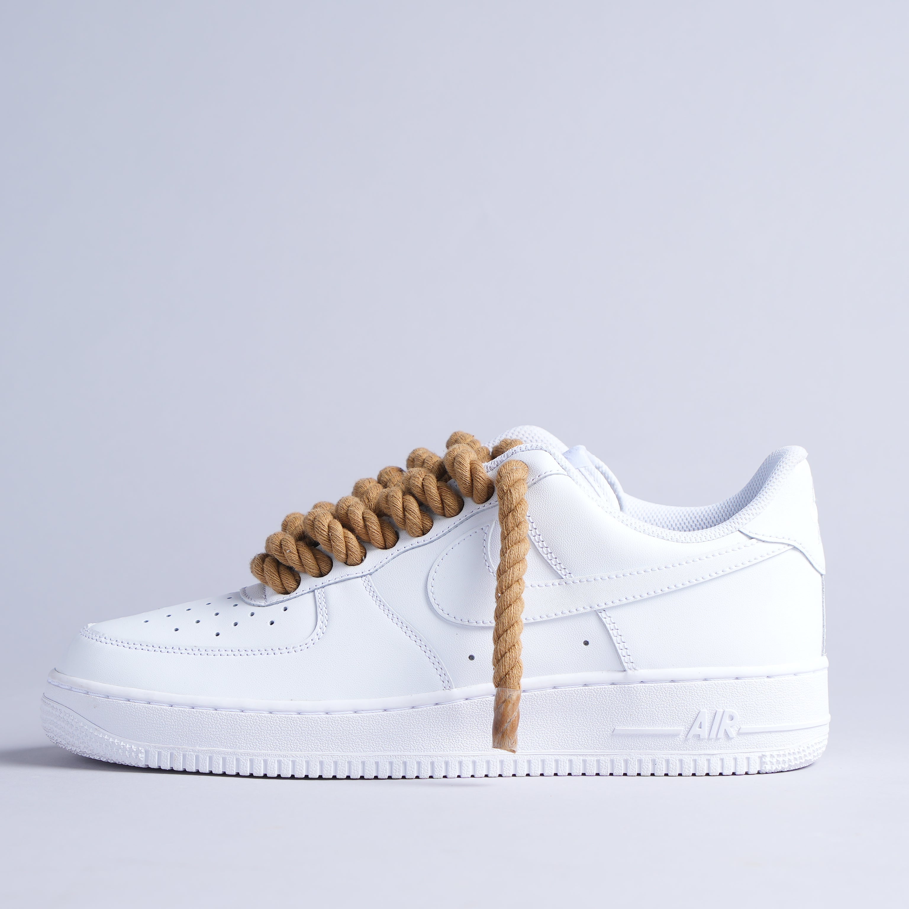 White leather sneaker with oversized tan rope laces on a light gray background