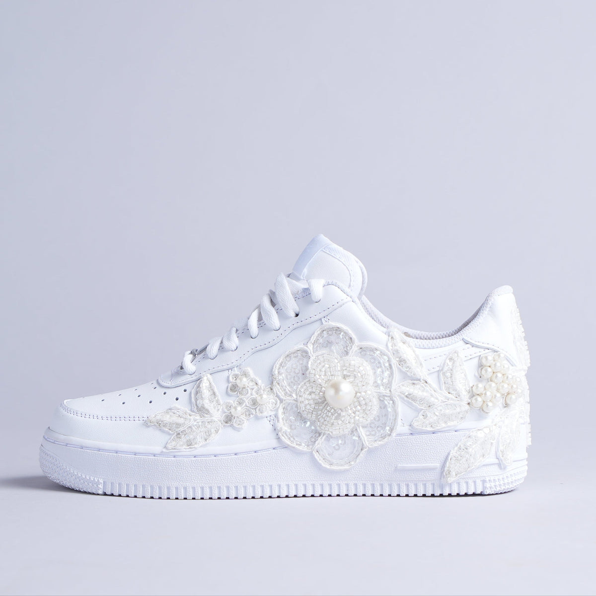 White low-top sneaker with pearl and beaded floral embellishments on a plain background
