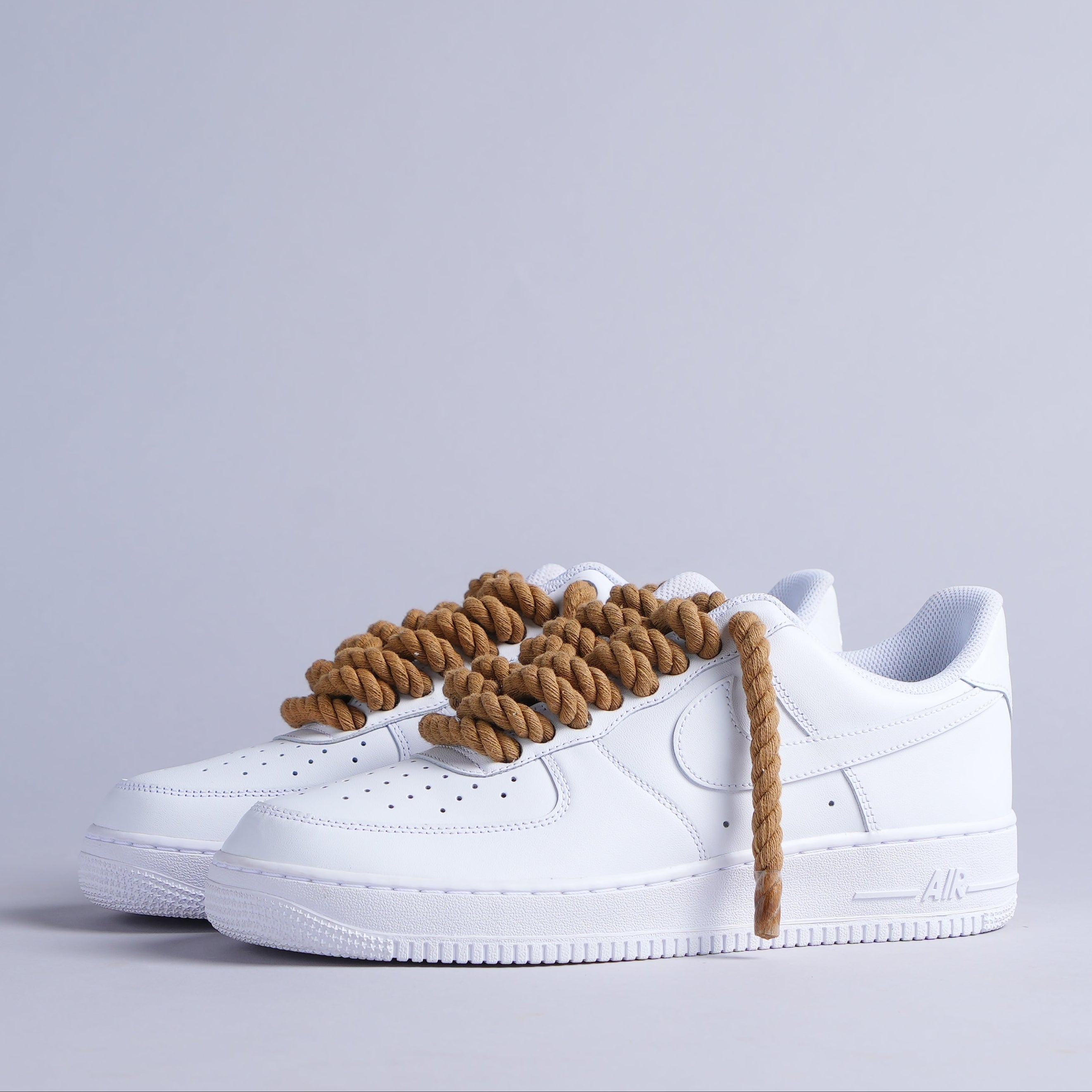 White streetwear sneakers with thick brown rope laces on a neutral background