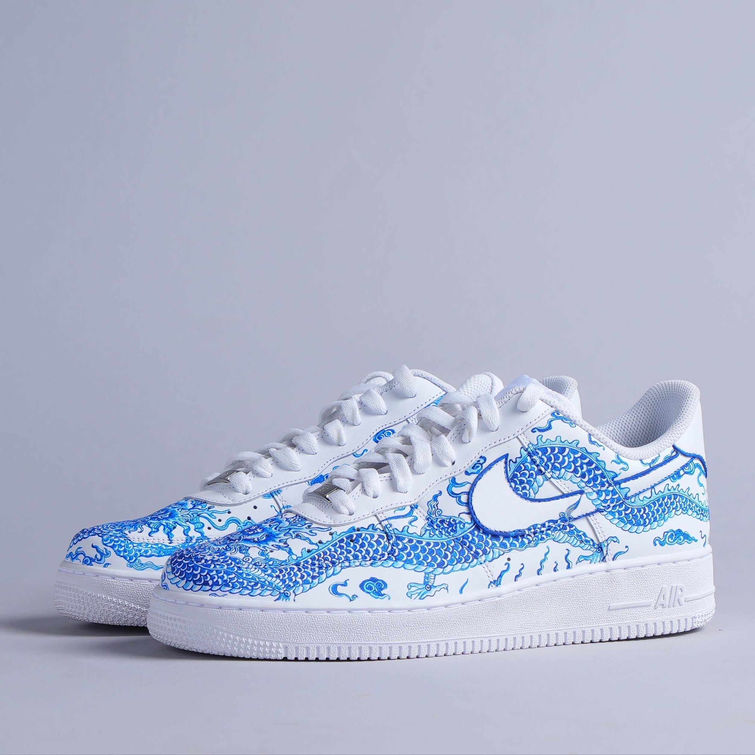 White low-top sneakers with blue dragon design on side, streetwear style, studio background