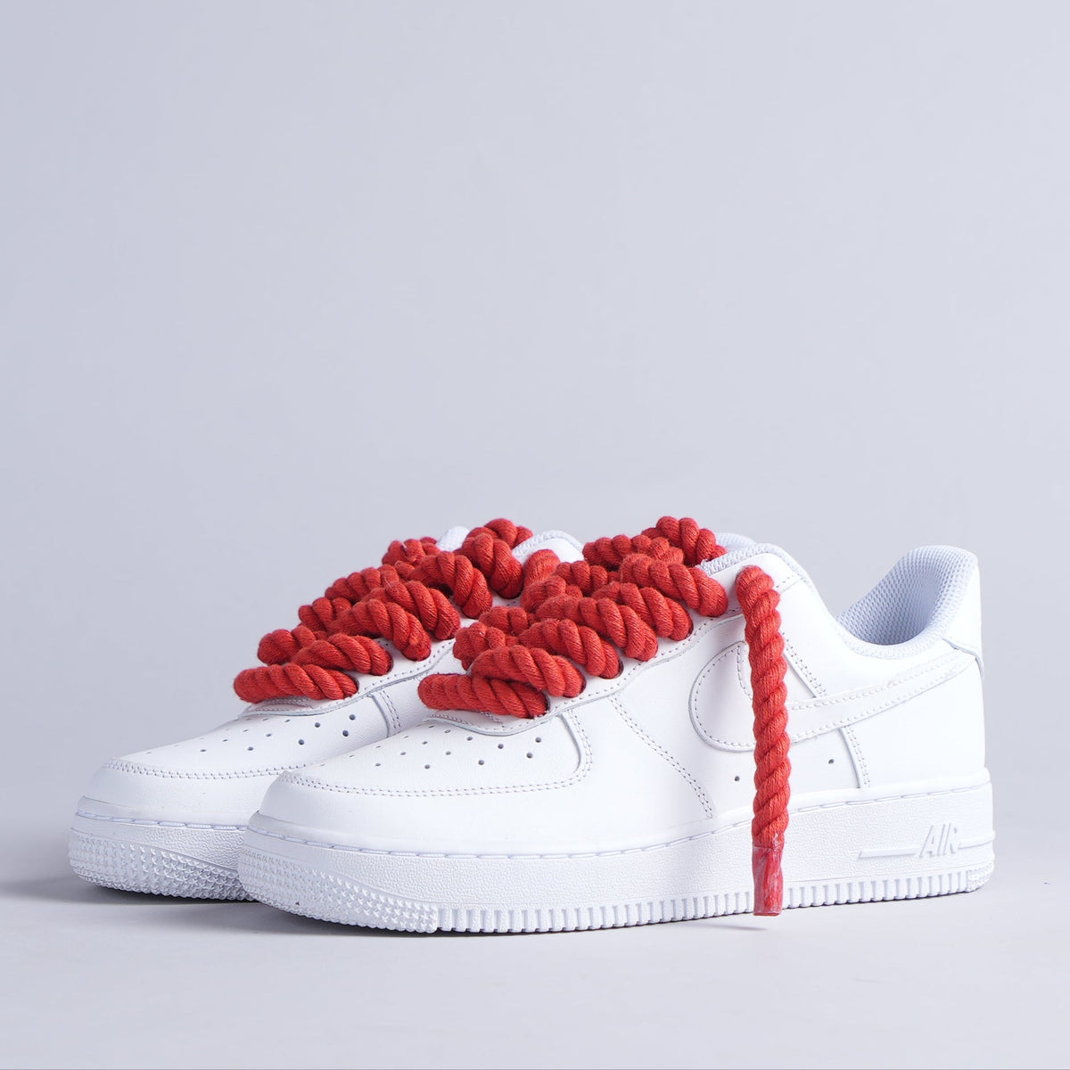 White low-top sneakers with thick red rope laces on a light grey background.