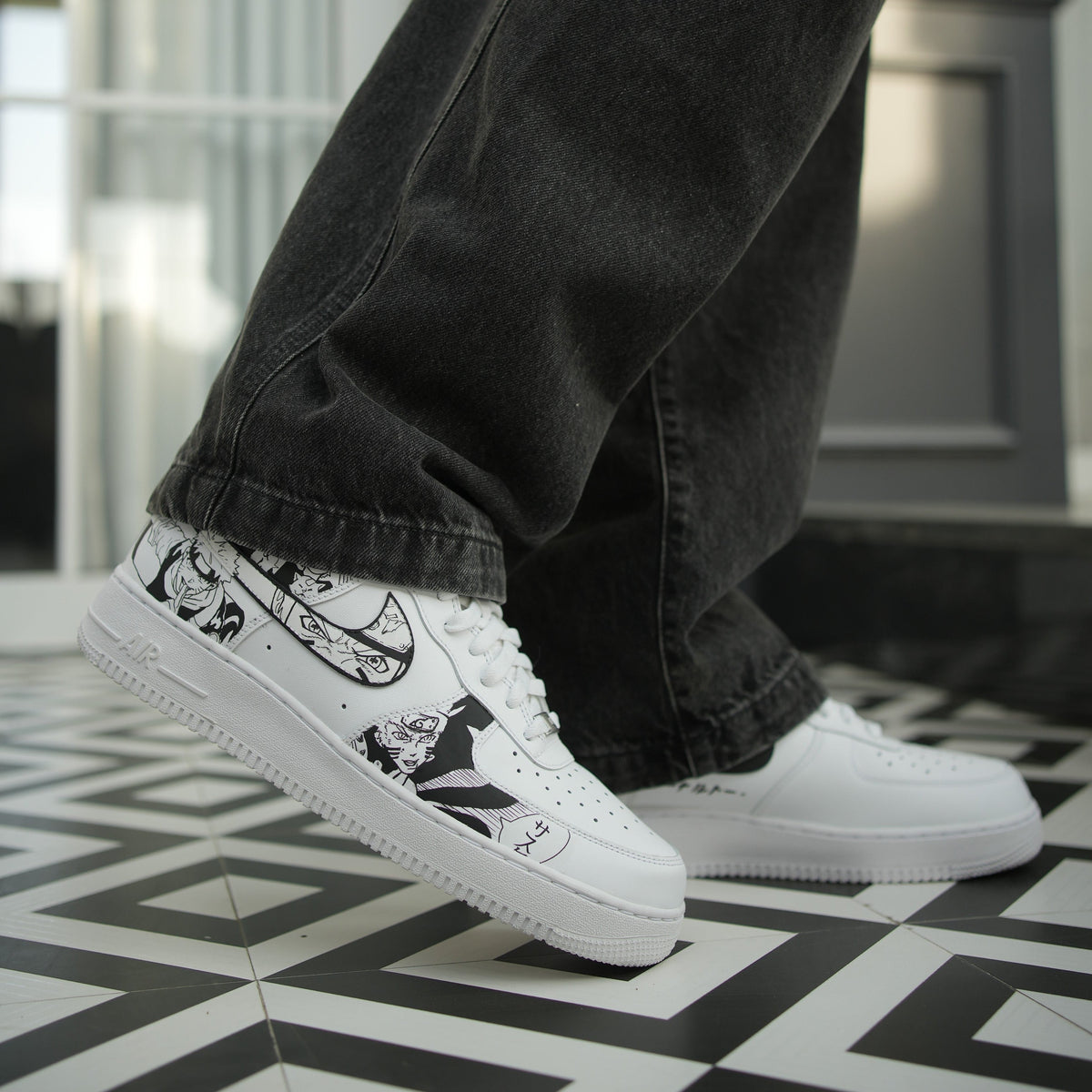 White custom streetwear sneakers with black anime graphics, worn with black jeans on a geometric tile floor