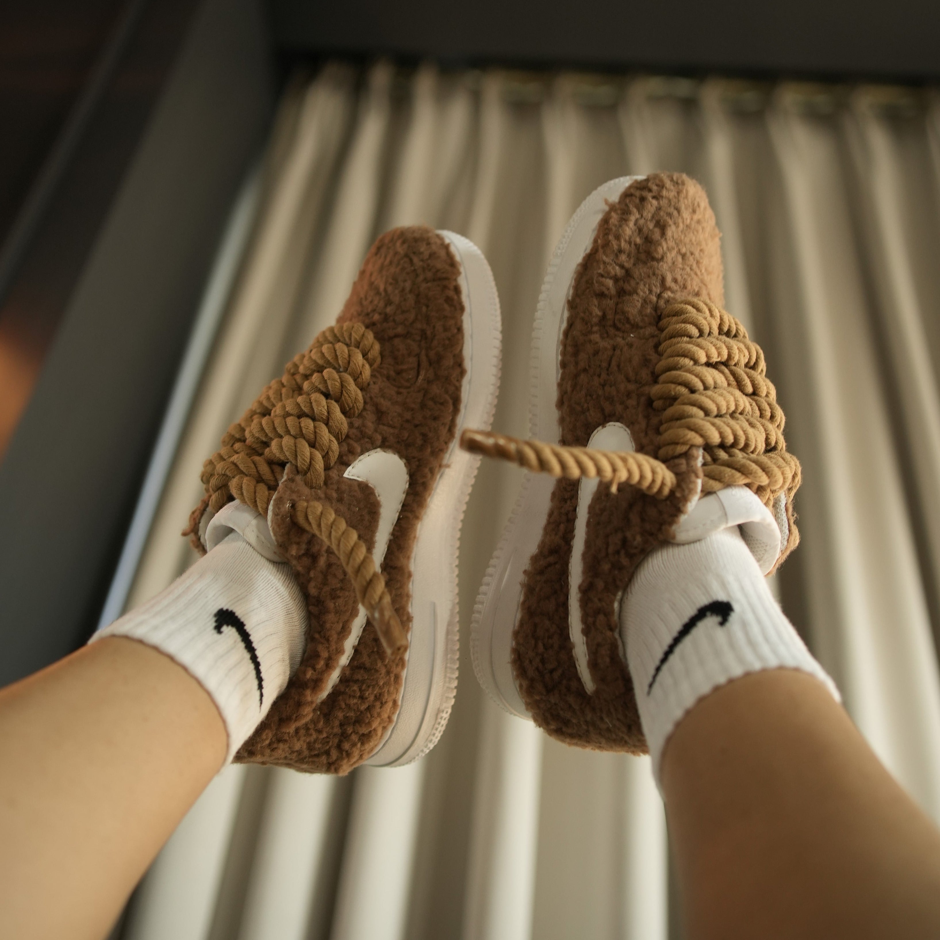 Brown sherpa sneakers with chunky rope laces, white swoosh and sole, worn with white socks