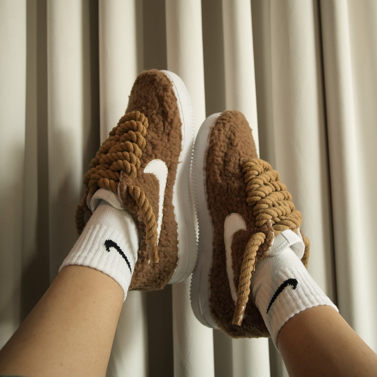 Brown fuzzy sneakers with thick rope laces and white swoosh, worn with white socks.