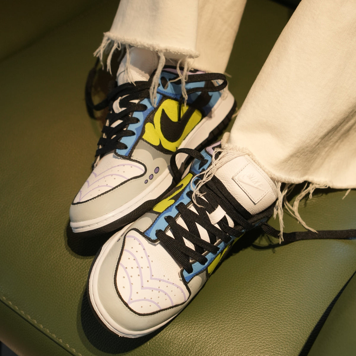 Colorful Nike Dunk sneakers with graphic patterns and frayed white jeans on green seat