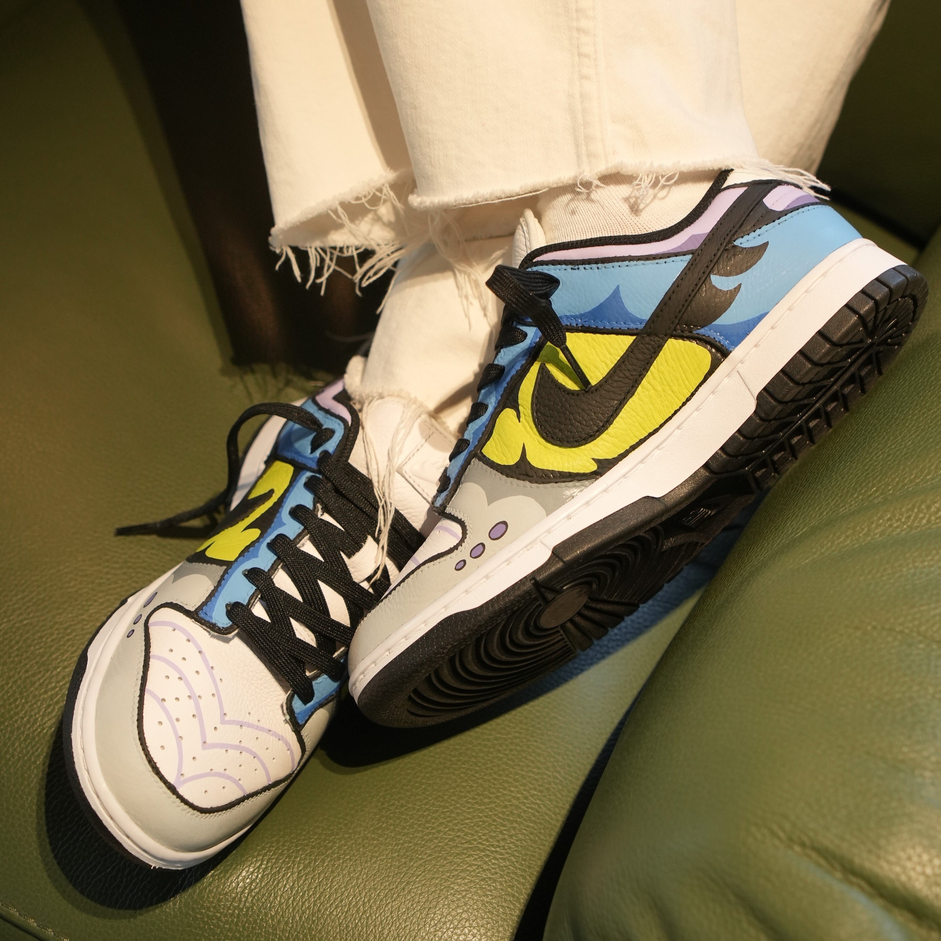 Colorful Nike Dunk sneakers with cartoon-style patterns and black swoosh, worn with white jeans.