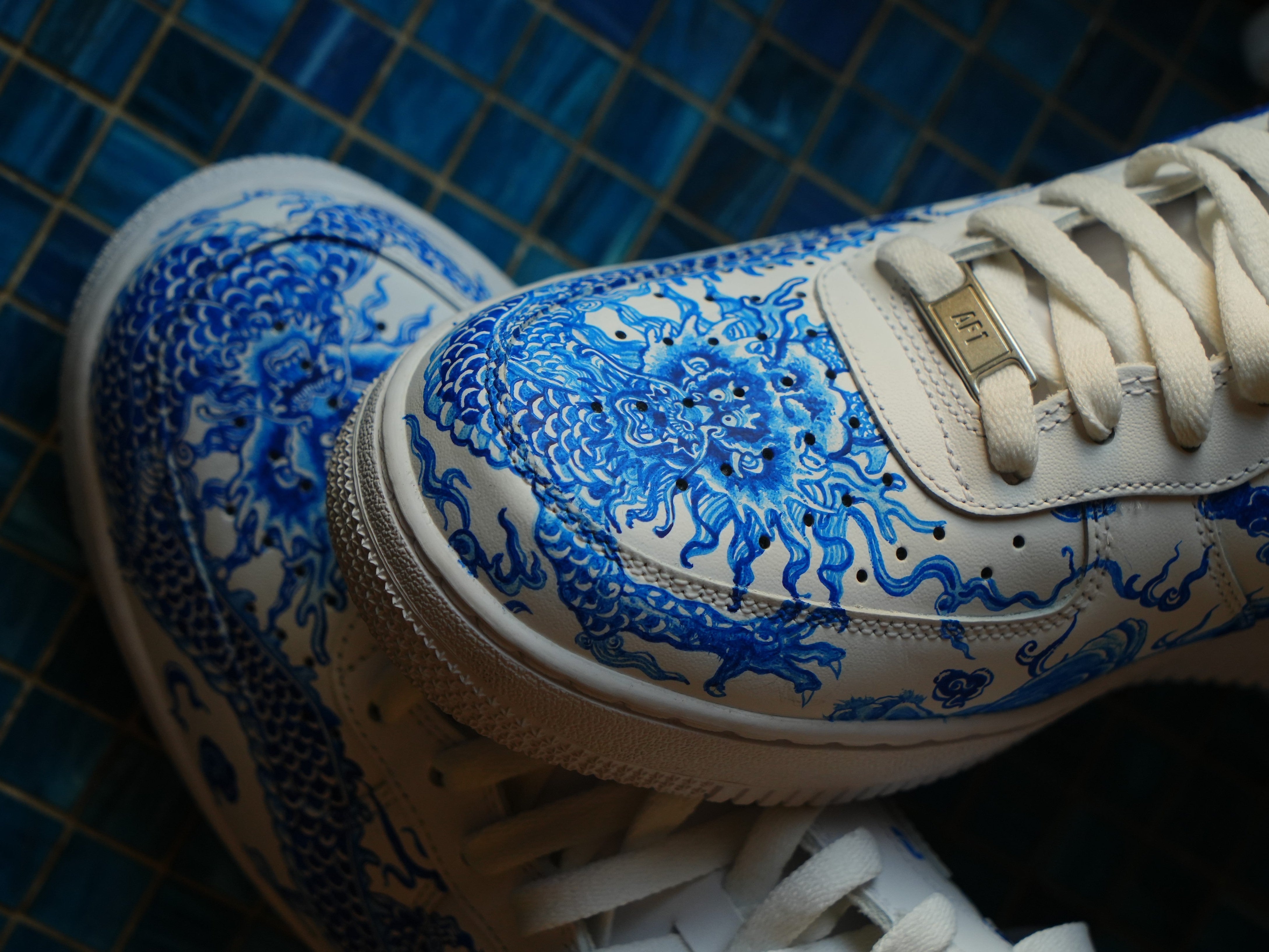 White sneakers with blue dragon design on tiled background, streetwear style footwear
