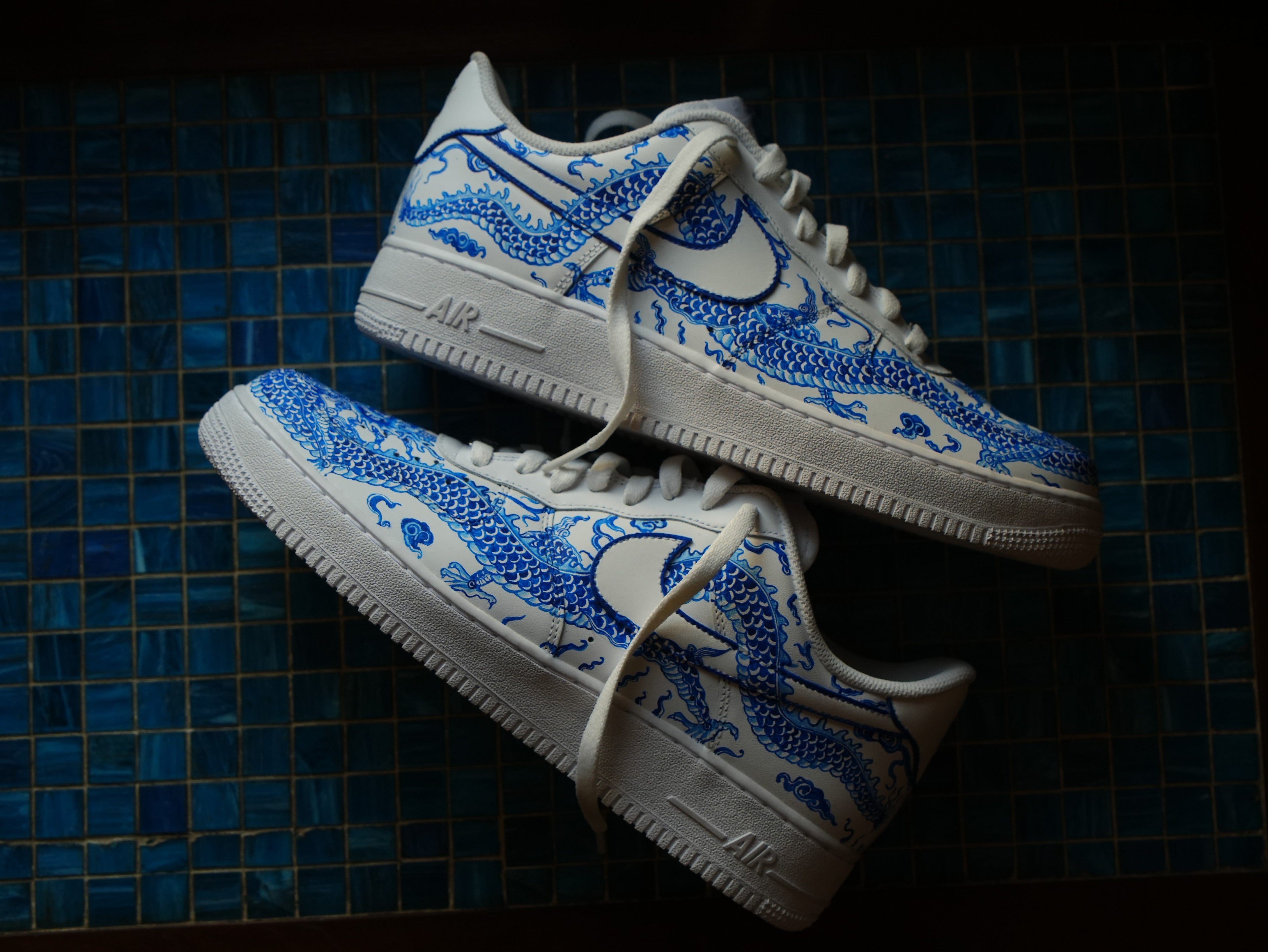 White sneakers with blue dragon design on a blue tiled background, streetwear footwear
