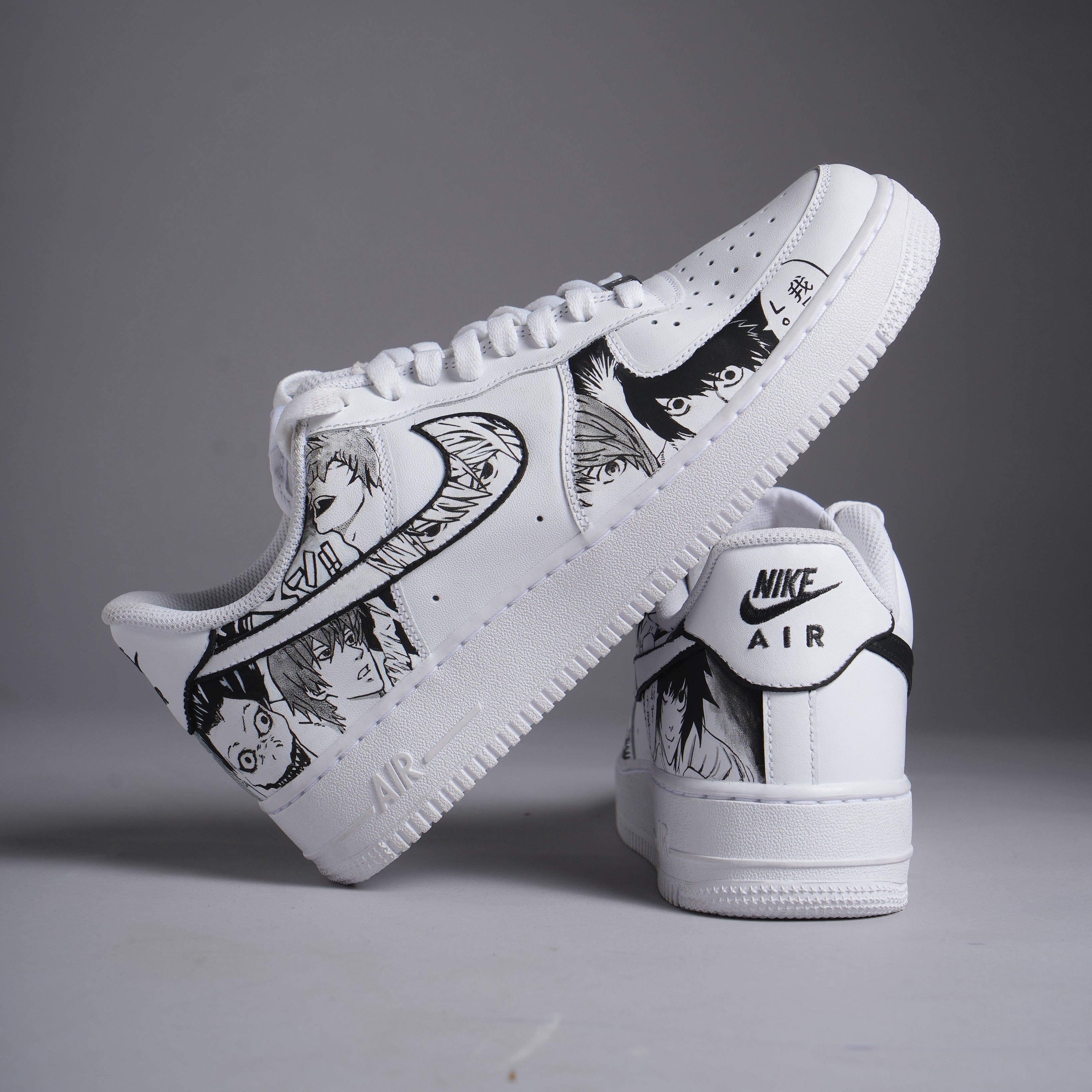 White Nike Air Force 1 sneakers with custom black anime character illustrations, displayed on gray background.