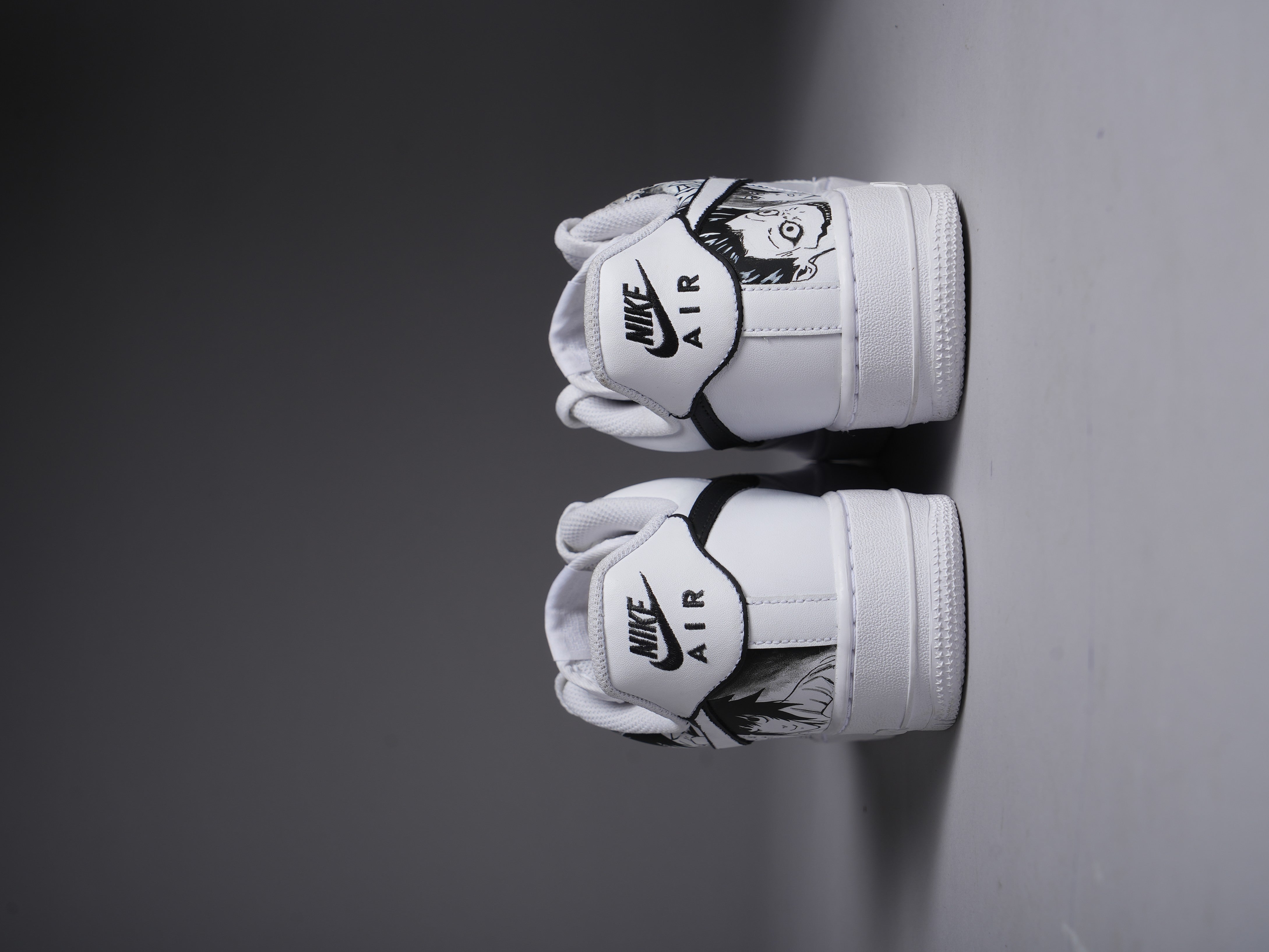 White Nike Air Force 1 sneakers with custom black graphic art on the heels, streetwear style
