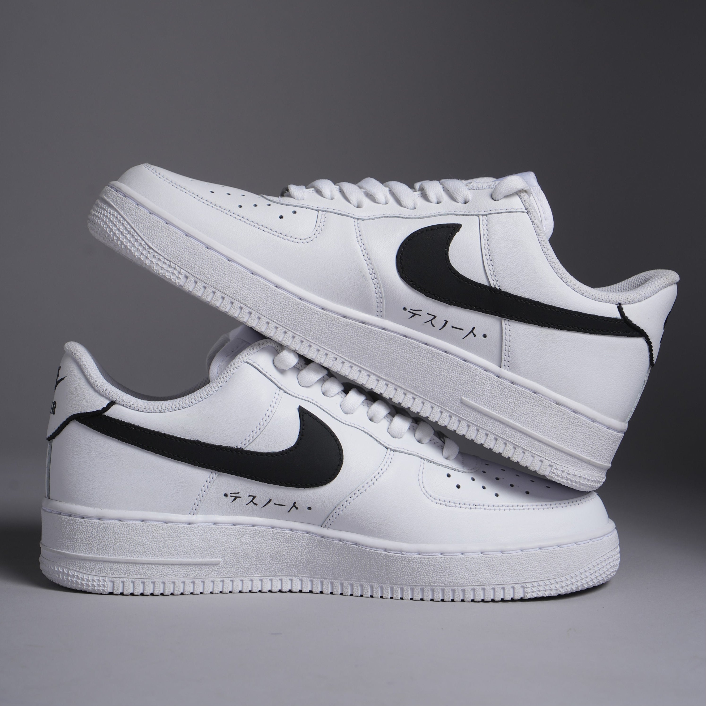 White low-top sneakers with black swoosh, Japanese text, streetwear style on gray background