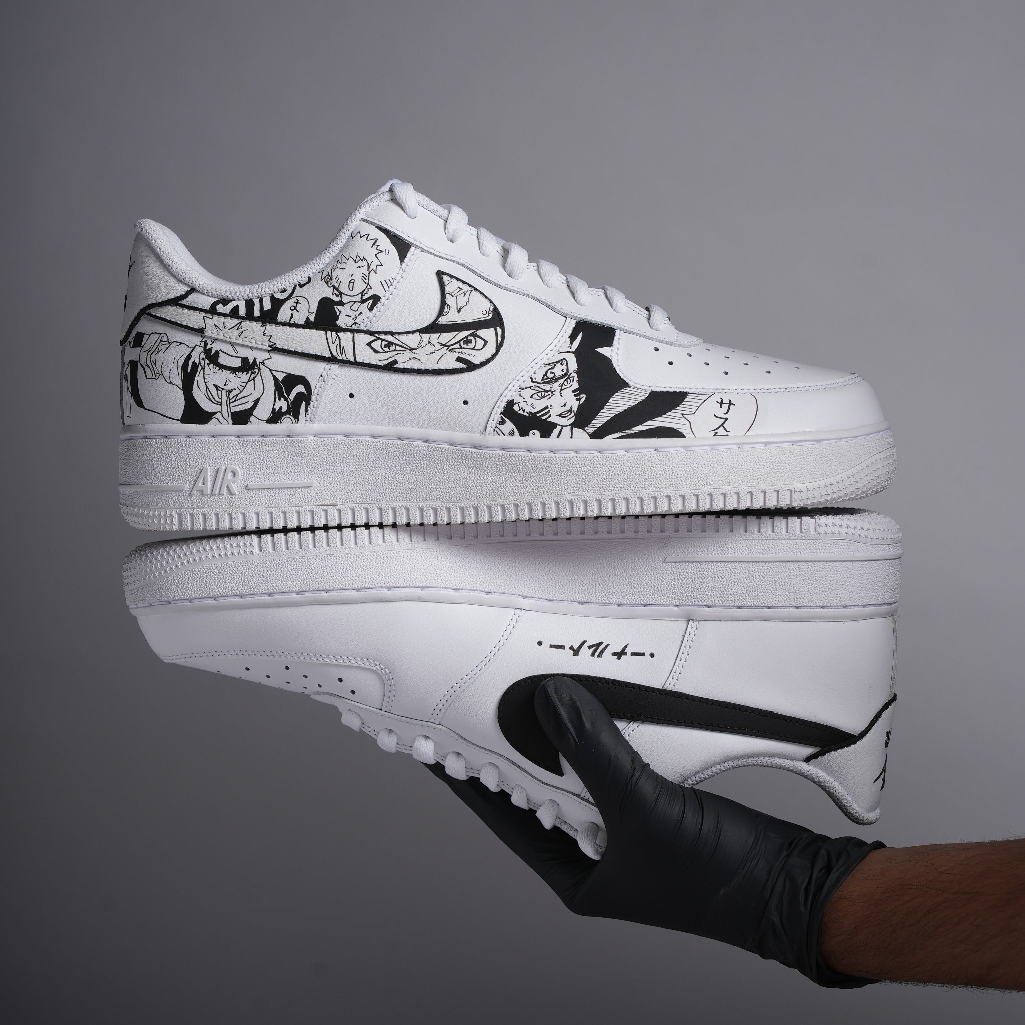 Custom white sneakers with black anime artwork, held by gloved hand against gray background