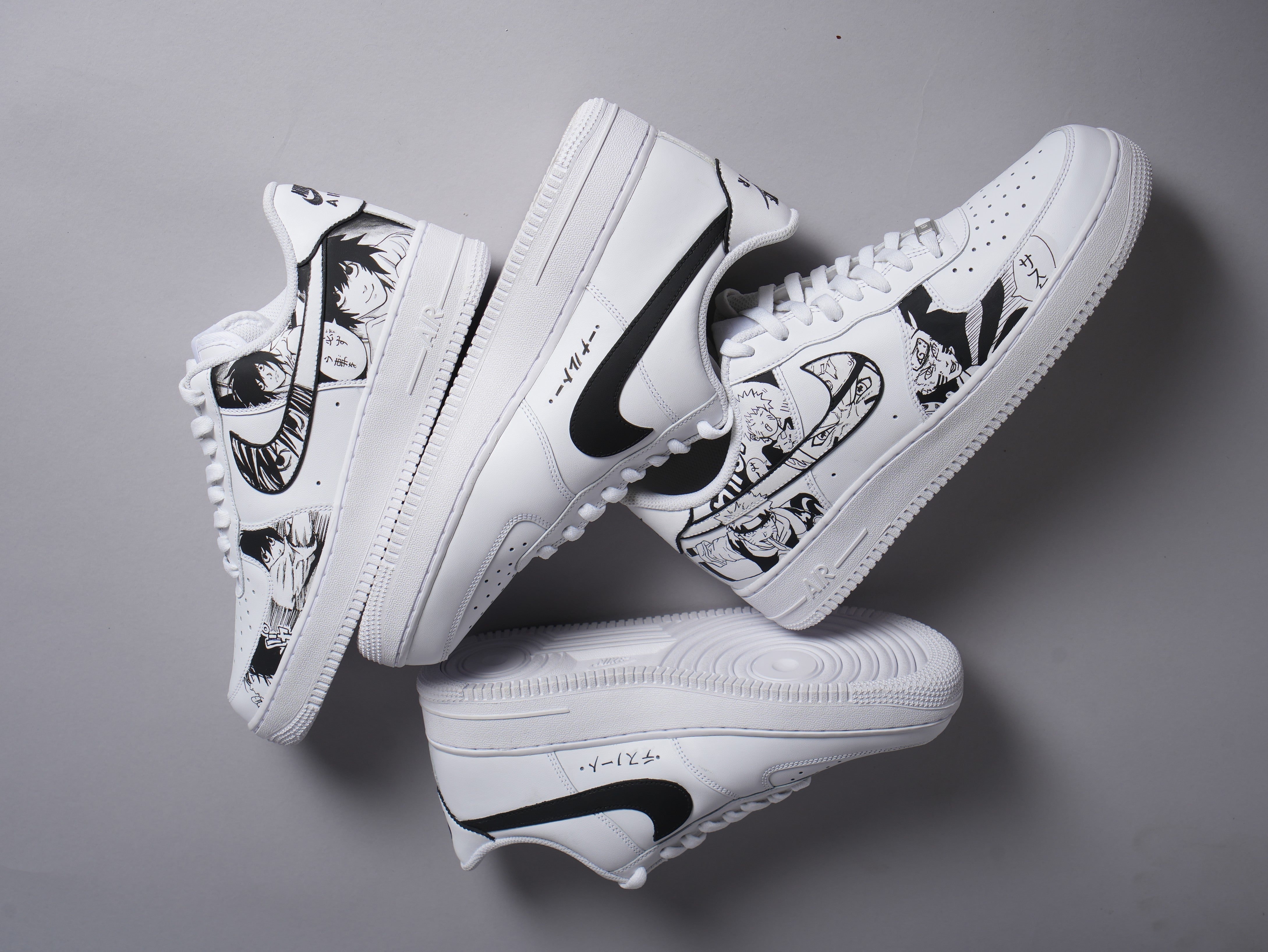 White streetwear sneakers with black anime-inspired artwork and bold swoosh design on gray background.