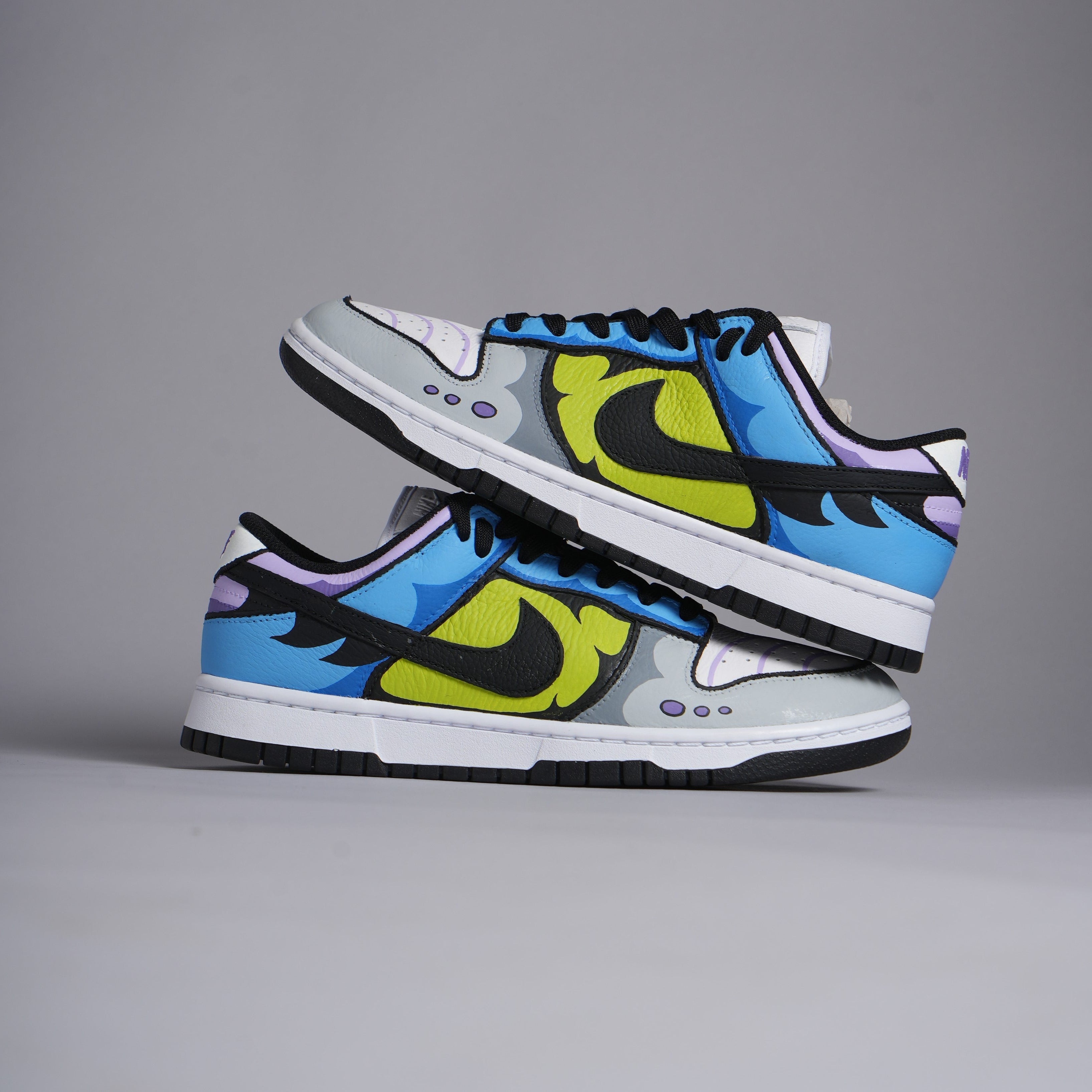 Colorful Nike Dunk Low sneakers with blue, yellow, black, and purple graphic design on studio background