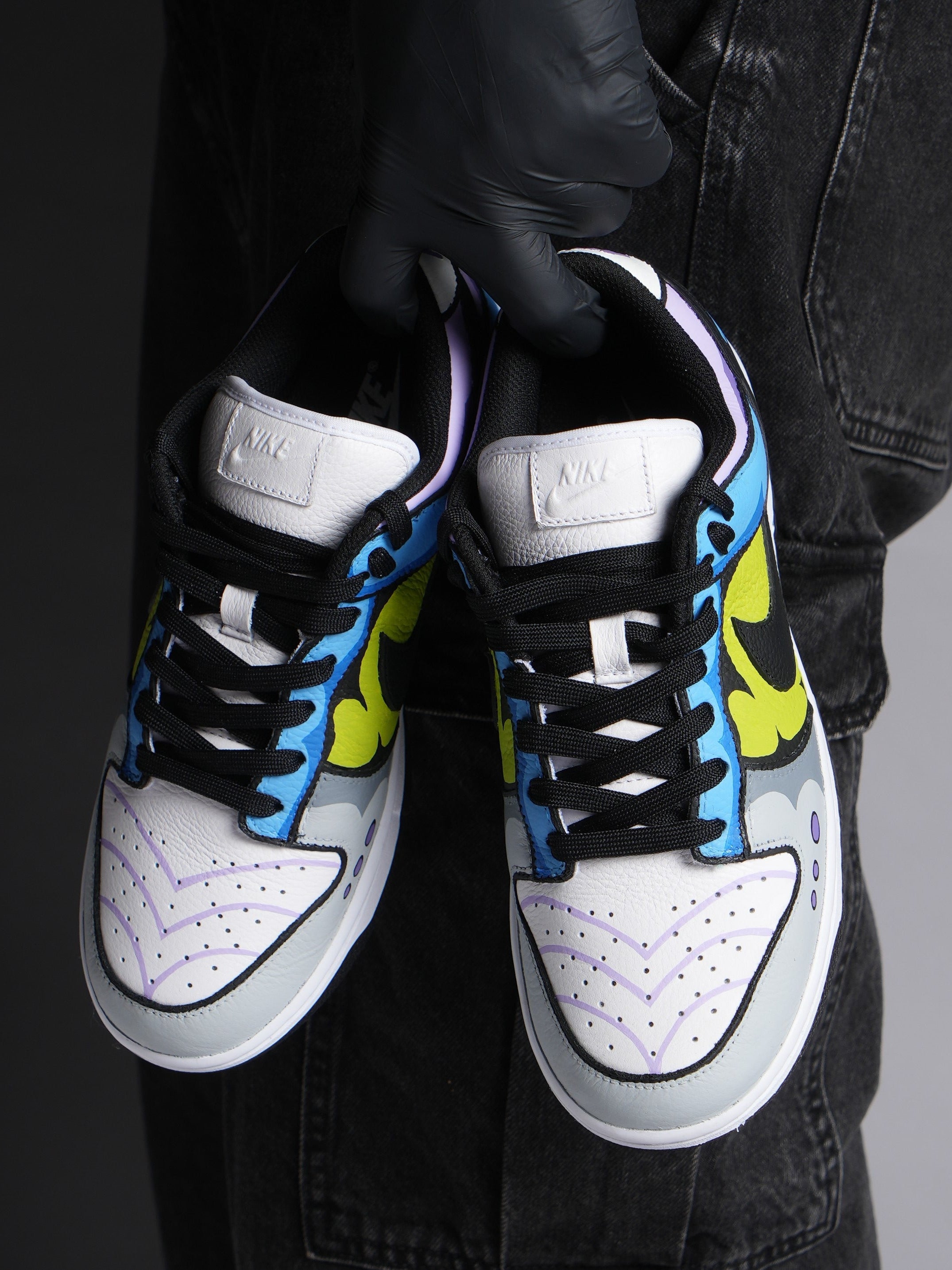 Hand holding custom Nike sneakers with bold blue, yellow, and purple streetwear design.