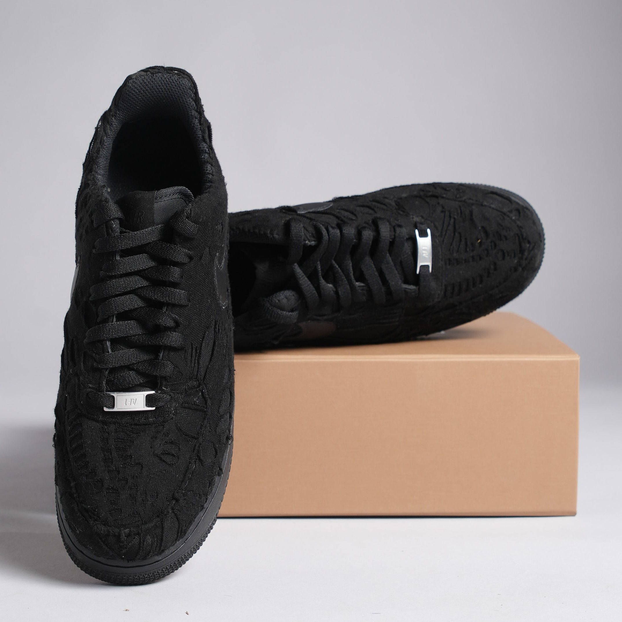 Black textured streetwear sneakers with floral embroidery on a brown shoe box, luxury footwear