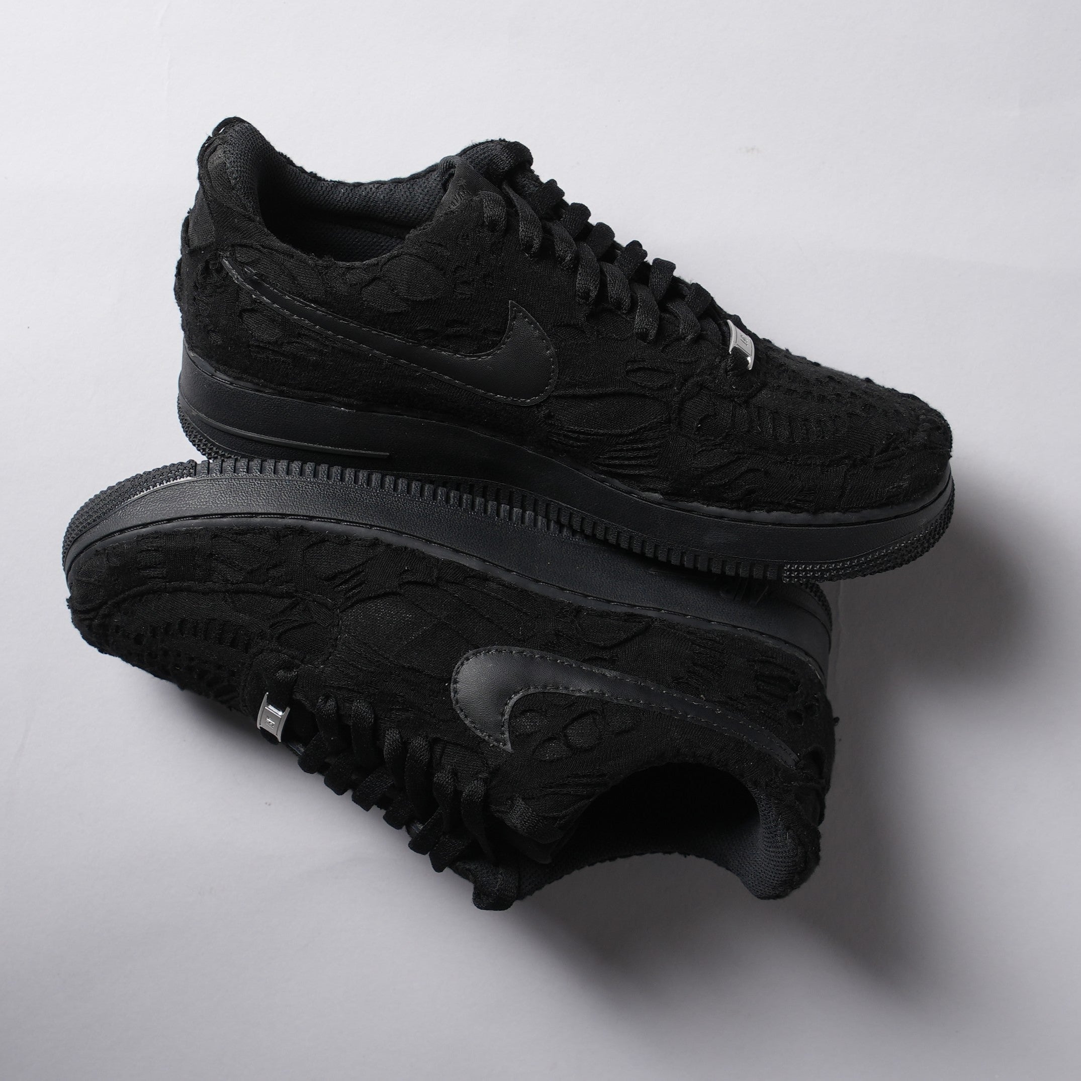 Black textured low-top sneakers with embossed patterns and tonal Swoosh logo on white background
